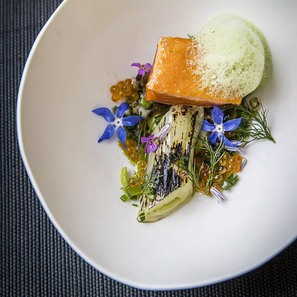 Assiette de nourriture gastronomique avec une tranche de poisson, légumes grillés, œuf en gelée verte, fleurs comestibles et gel de sauce