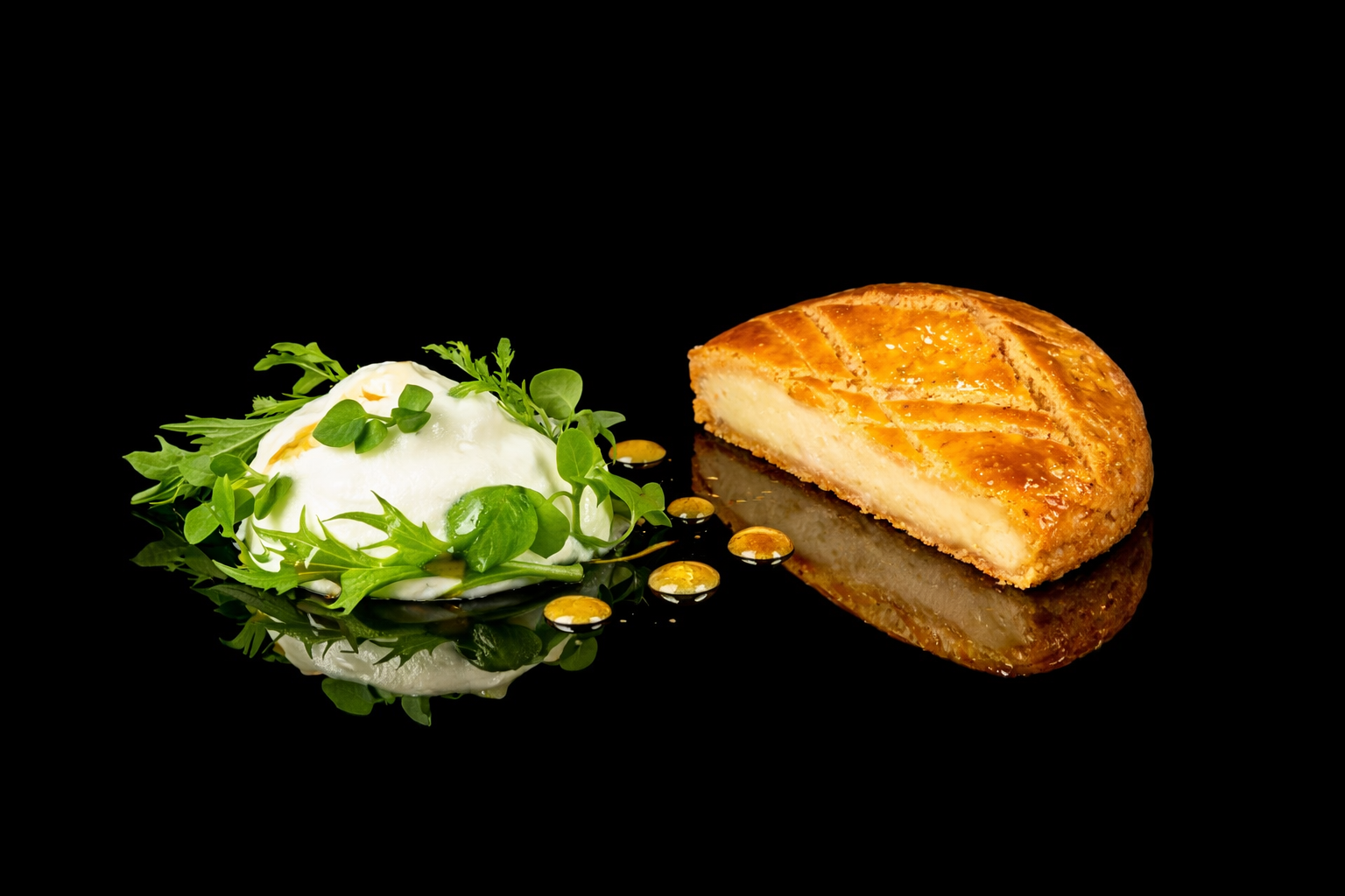 Partie de tarte au fromage avec un côté glacé à la crème, garnie de microvertes, et accompagnée de gouttes de sauce sur une surface noire reflective.