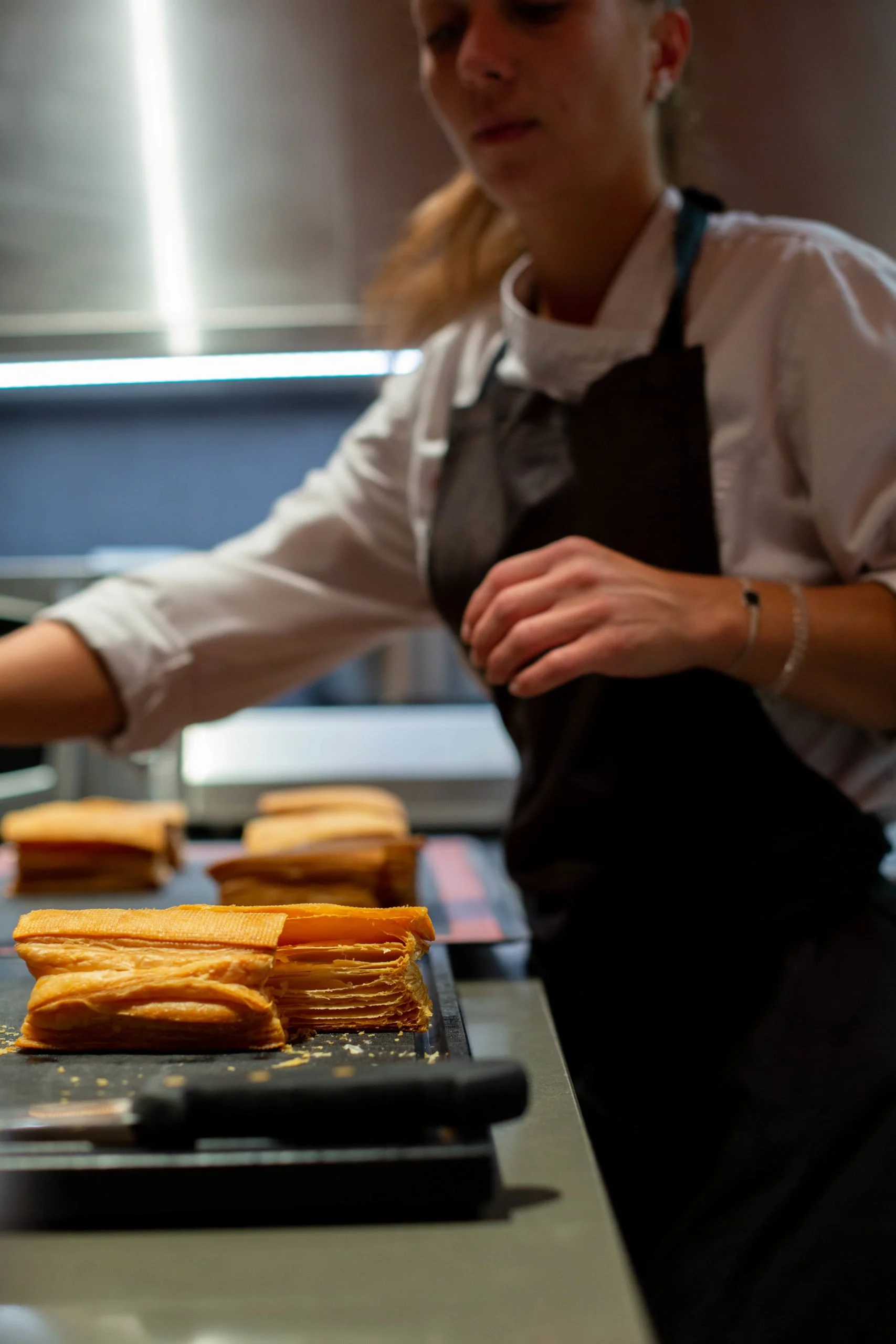 Une pâtissière prépare des mille-feuilles dans une cuisine.