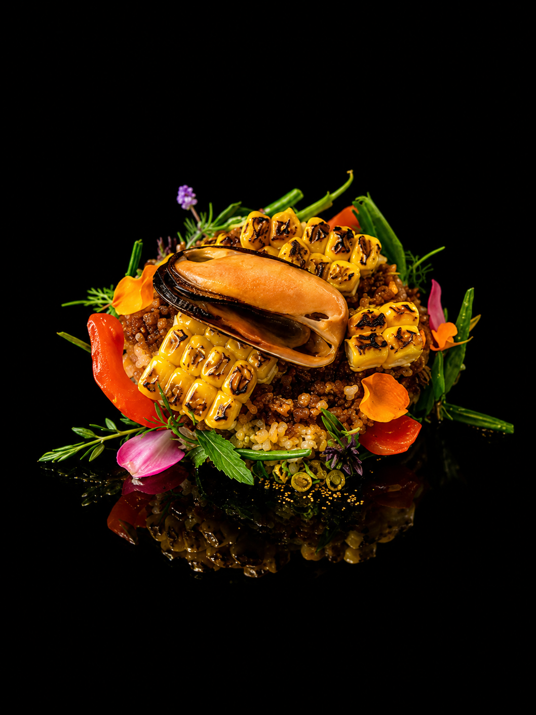 Assiette de riz garnie de coquillage, maïs, légumes verts, fleurs comestibles et herbes.