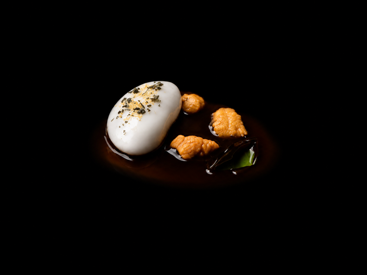 Assiette gastronomique avec un œuf roulé, garnitures en sauce, et une petite feuille verte, sur un fond noir.