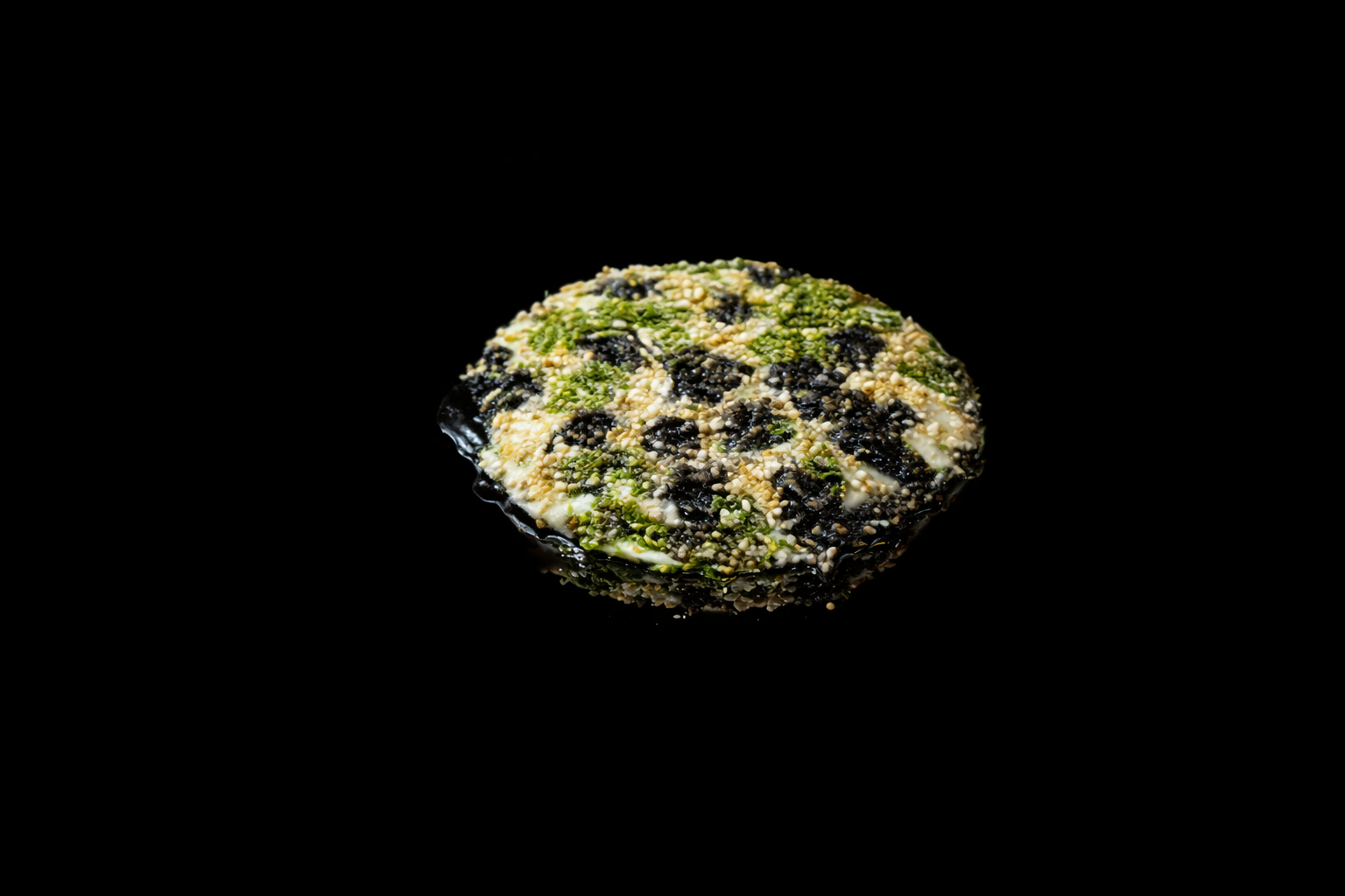Un rond de sushi garni de graines de sésame, de thon, et d'autres ingrédients, posé sur un fond noir