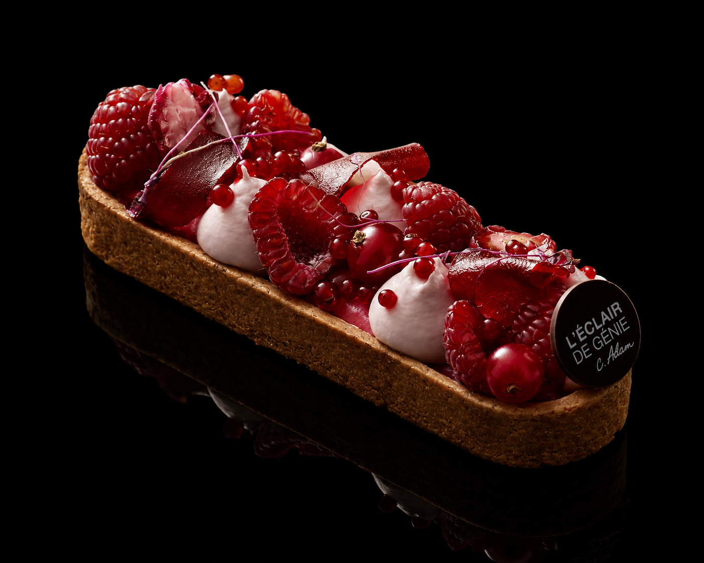 Gâteau décoré de fruits rouges, sauce rouge, et crème, avec un fond noir.