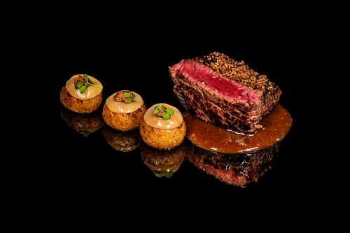 Assiette avec trois petits amuse-bouches et un morceau de steak cru, sur une surface noire.