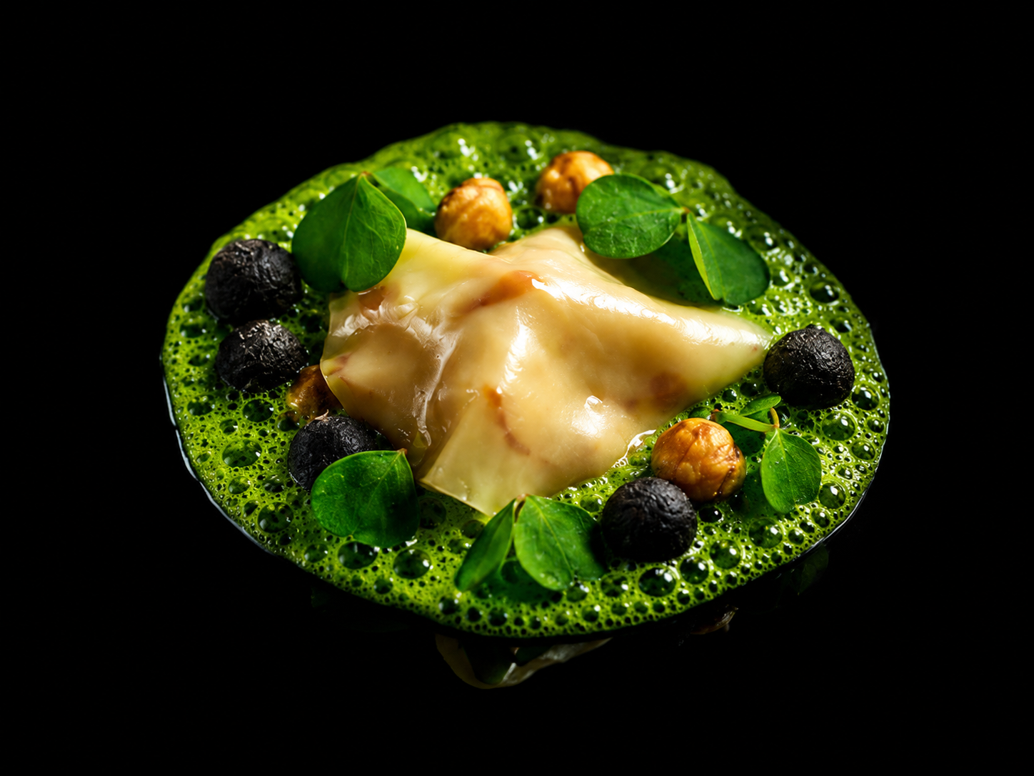 Assiette de fromage avec un tube de fromage fondu, accompagnée de myrtilles, de noisettes et de feuilles vertes, dans un fond noir.