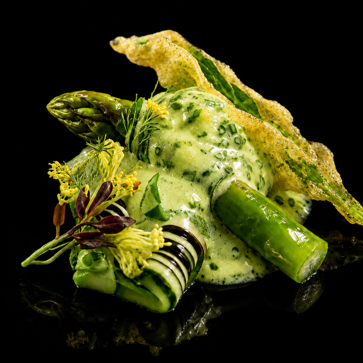 Création culinaire artistique avec des éléments de légumes verts, garnie de sauce verte, fleurs comestibles, feuilles et feuilles de plantes vertes, présentation élégante sur un fond noir.