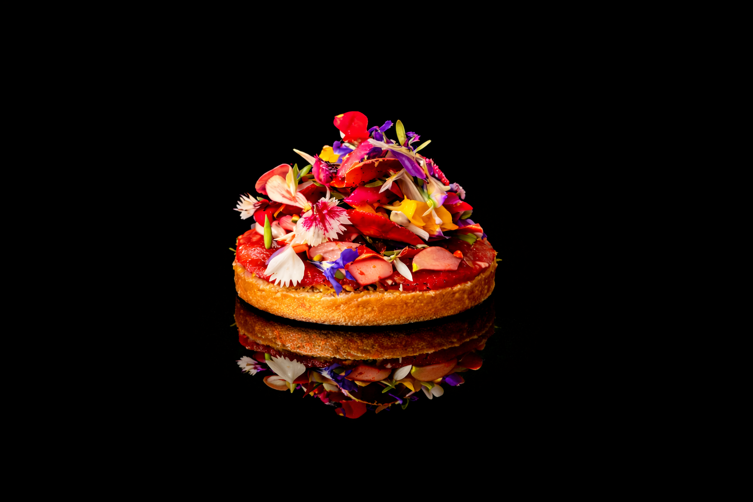 Tarte aux fruits décorée de fleurs comestibles sur fond noir.
