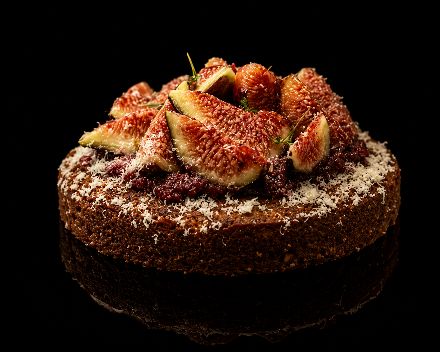 Gâteau au fond de tarte garni de figues fraîches, de fromage râpé et de petites herbes, présenté sur un fond noir.