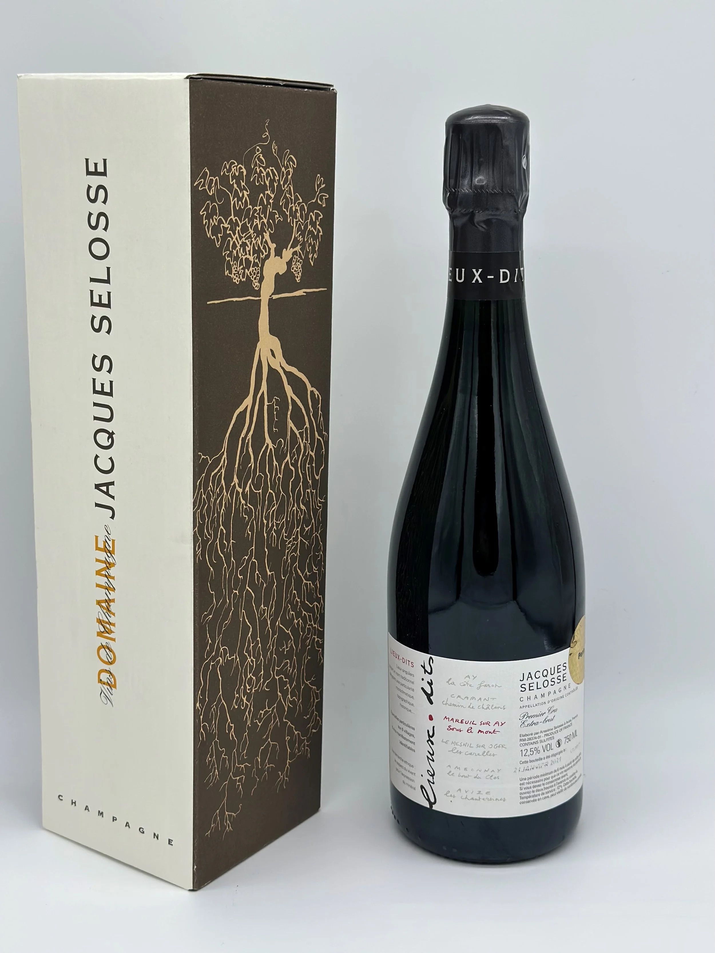 Une bouteille de champagne Jacques Selosse à côté de sa boîte d'emballage. La boîte est ornée d'une illustration d'arbre avec ses racines.