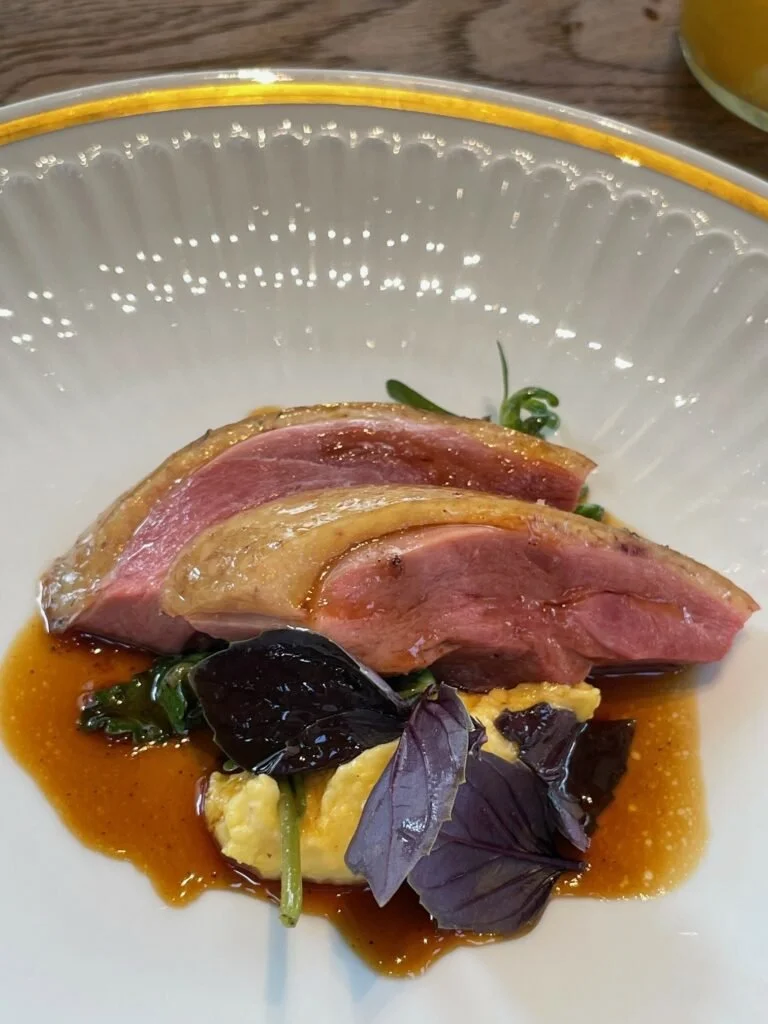 Filet de viande servi avec une sauce, des feuilles de basilic ou de menthe, et une purée ou une crème