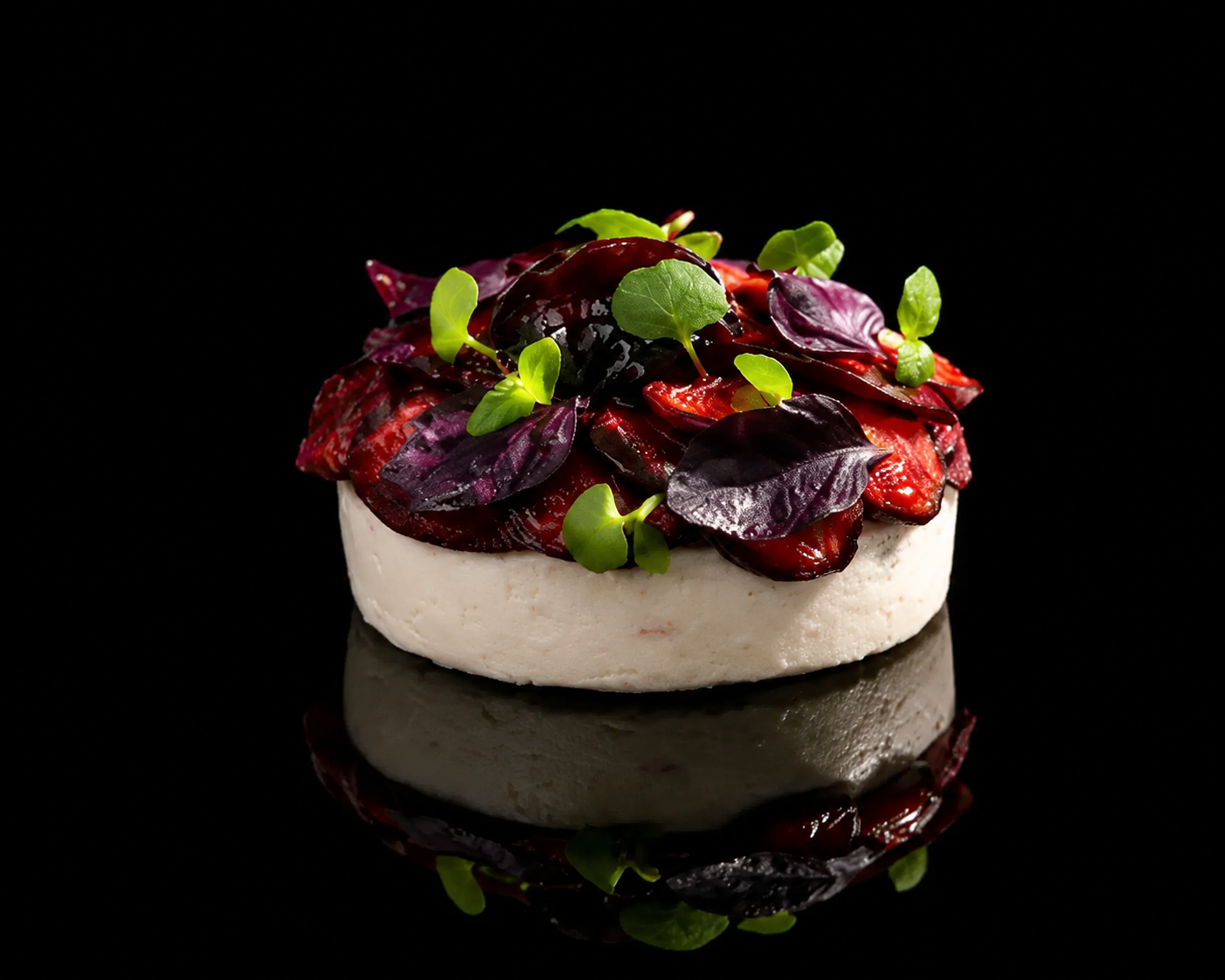 Une assiette de tartare de viande rouge garnie de feuilles vertes et violettes, sur un fond noir.