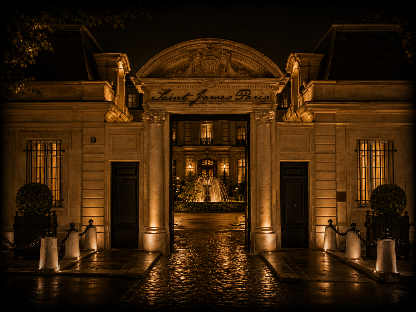Entrée éclairée d'un bâtiment avec un portail ouvert, vue vers une fontaine extérieure la nuit, inscription 'Saint James Paris' au-dessus de l'entrée.