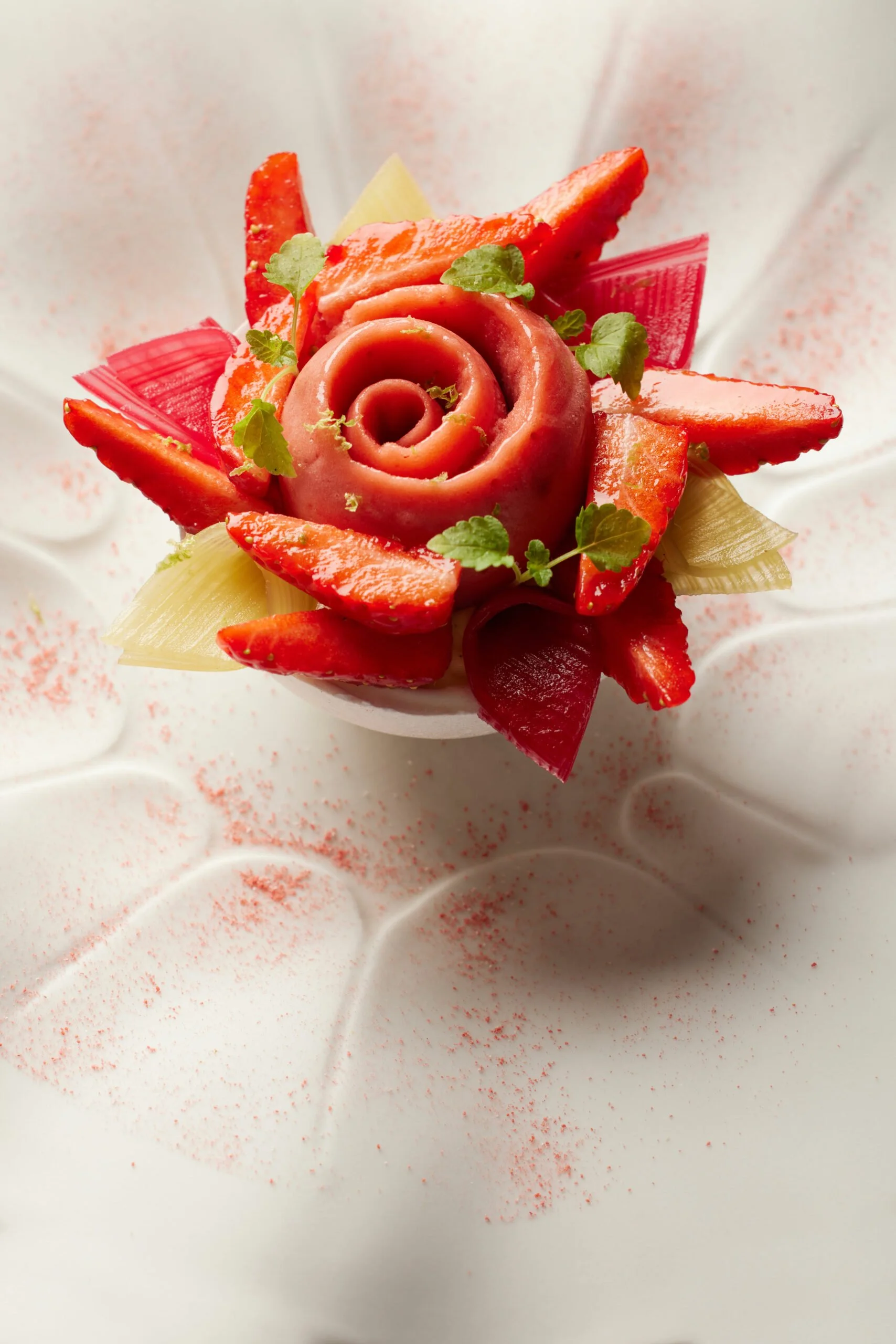 Une présentation artistique d'œufs durs décorés avec des tranches de légumes, dont des poivrons rouges, des céleris, et des feuilles de coriandre, formant une rose sur une assiette blanche garnie de poudre rouge.