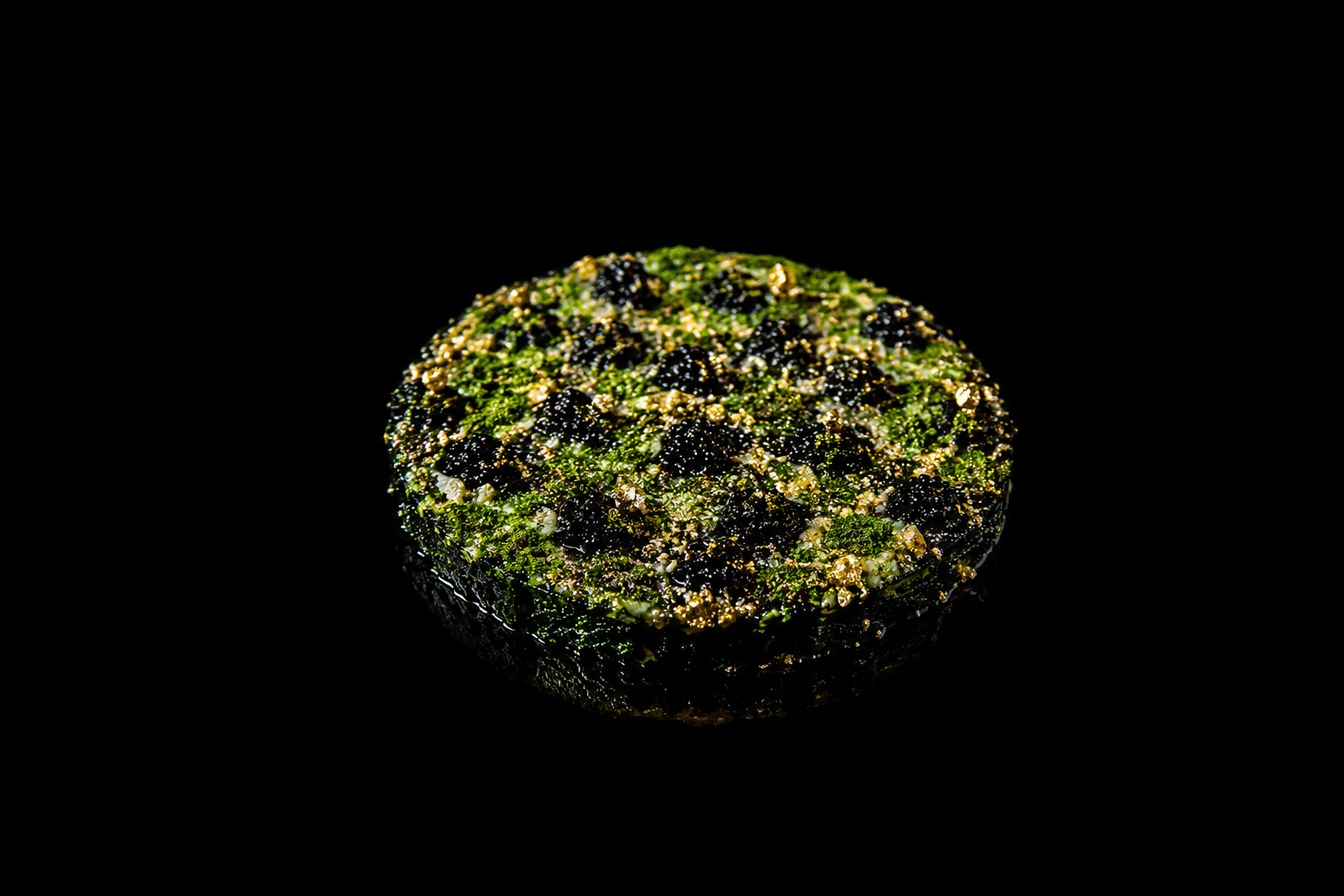 Un nigiri de yama gobo avec des graines de sésame et des garnitures noires et dorées, posé sur un fond noir.