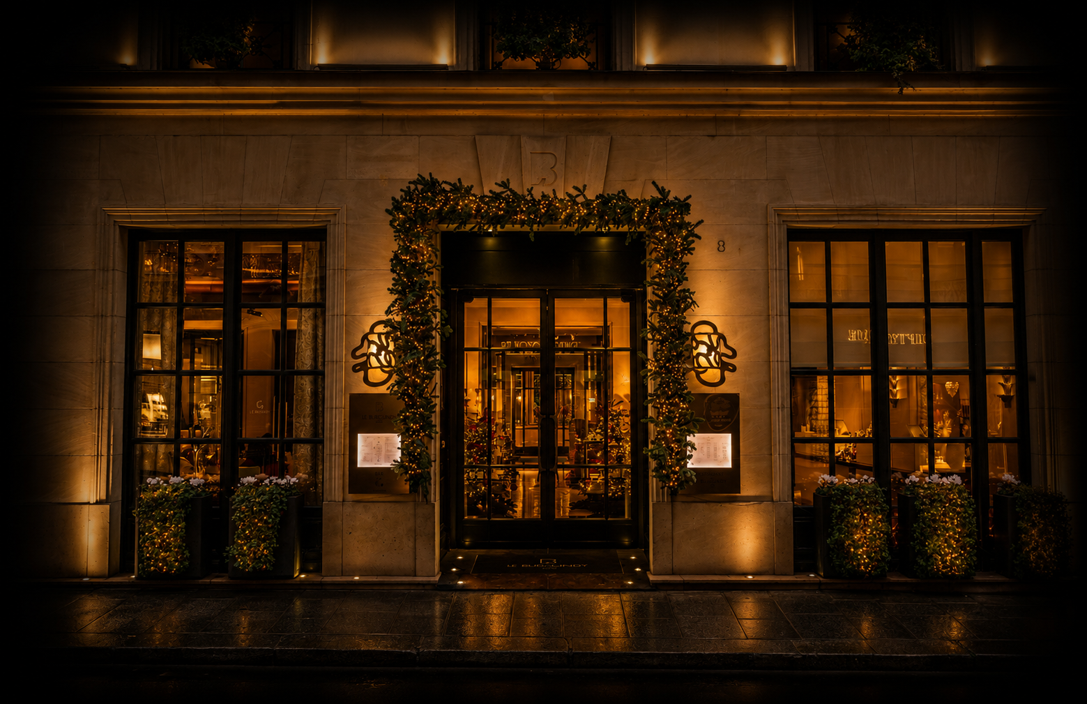 Façade d'un restaurant élégamment décorée pour Noël, avec des lumières chaudes, un cadre en sapin décoré de guirlandes lumineuses autour de la porte, et deux fenêtres illuminées, donnant une ambiance chaleureuse et festive.