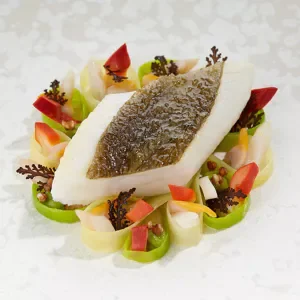 Poisson en croûte avec légumes décoratifs autour dans une assiette blanche.