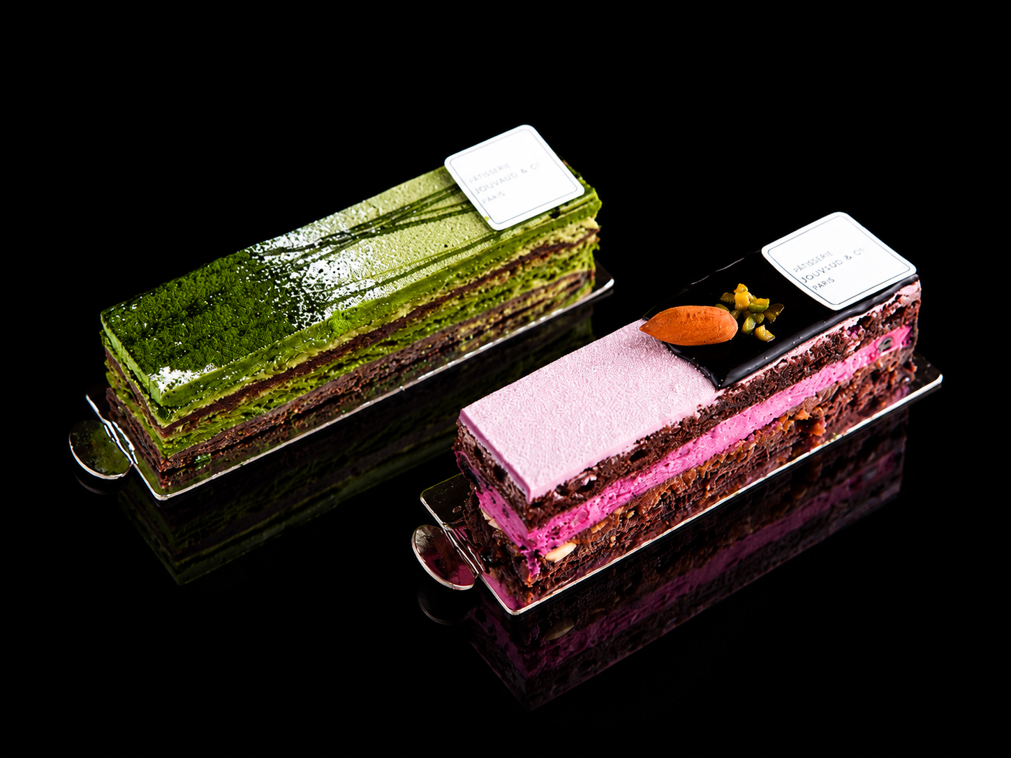 Deux pâtisseries rectangulaires élégantes avec glaçage décoratif et garnitures, placées sur un fond noir.