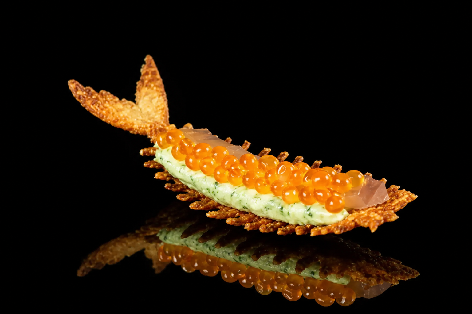 Amuse-bouche élégant avec une base de croustillant, garniture de crème verte, petites billes orange, et morceaux de poisson ou de gelée, posé sur une surface noire reflective.