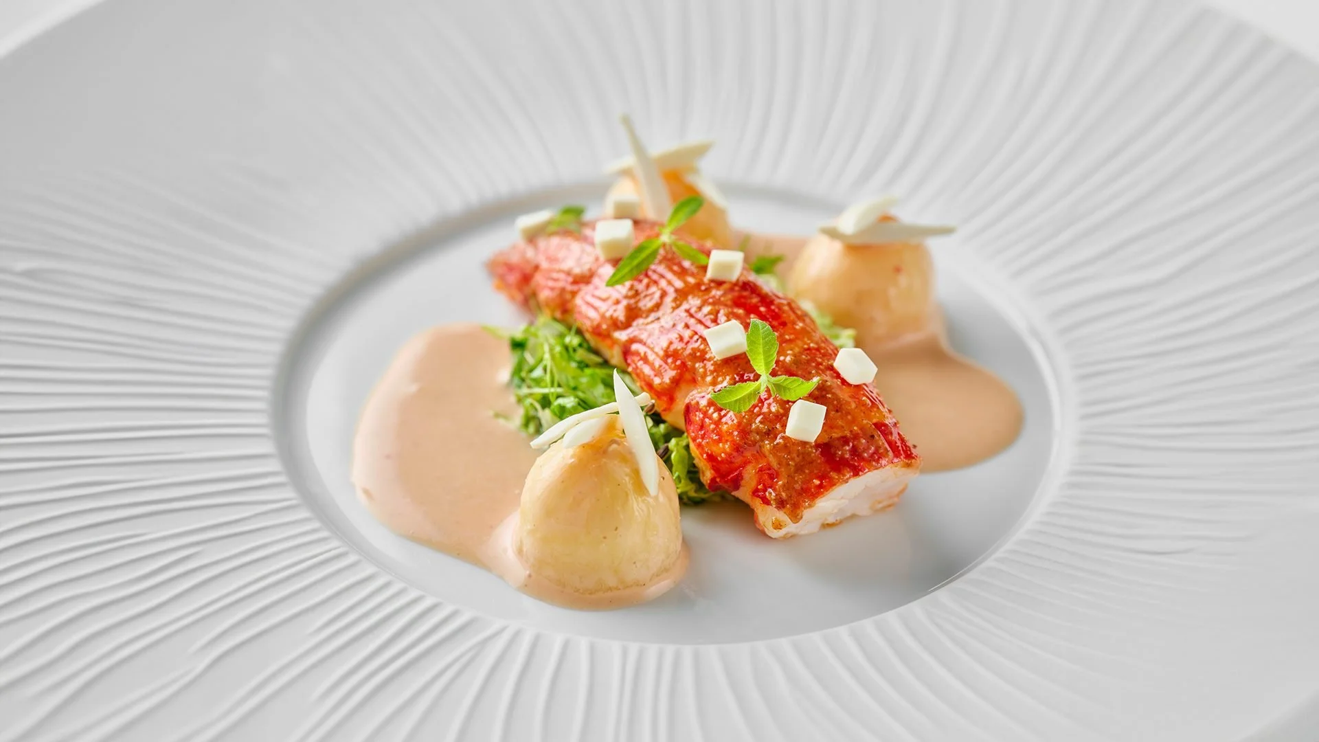 Filet de poisson avec sauce, légumes en garniture, et décoration végétale sur une assiette élégante.