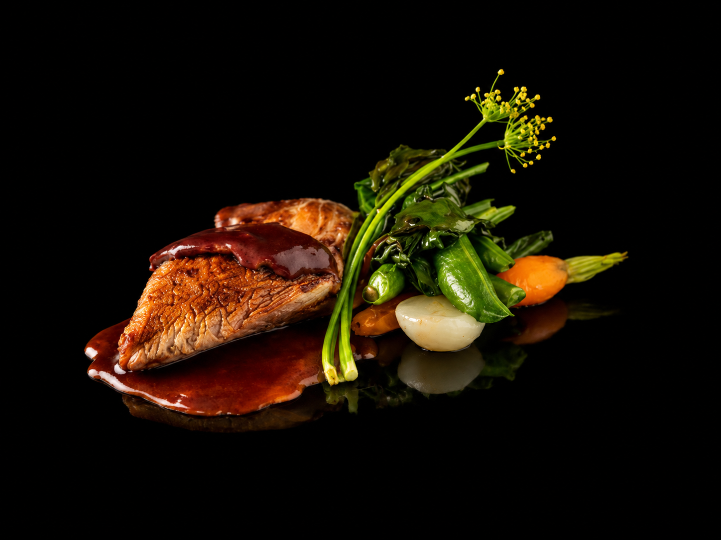 Deux morceaux de viande avec une sauce rouge accompagnés de légumes verts, carottes, oignons et une fleur jaune sur fond noir.