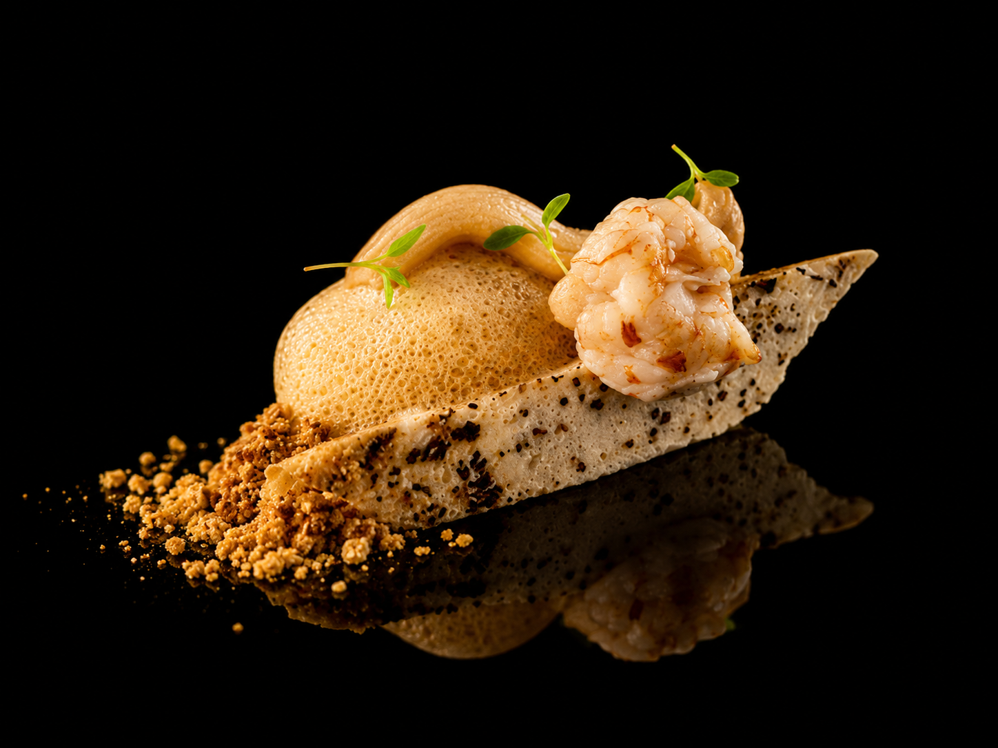 Assiette de crevettes avec espuma, crumble et garniture verte sur un fond noir