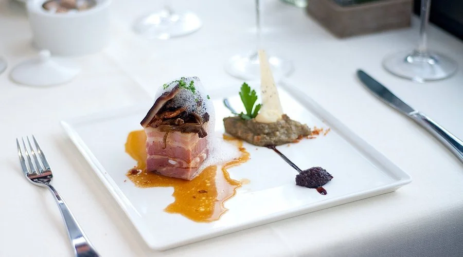 Assiette gastronomique avec un morceau de viande, accompagné d'une sauce, d'une purée et de fines herbes, dans un cadre élégant.
