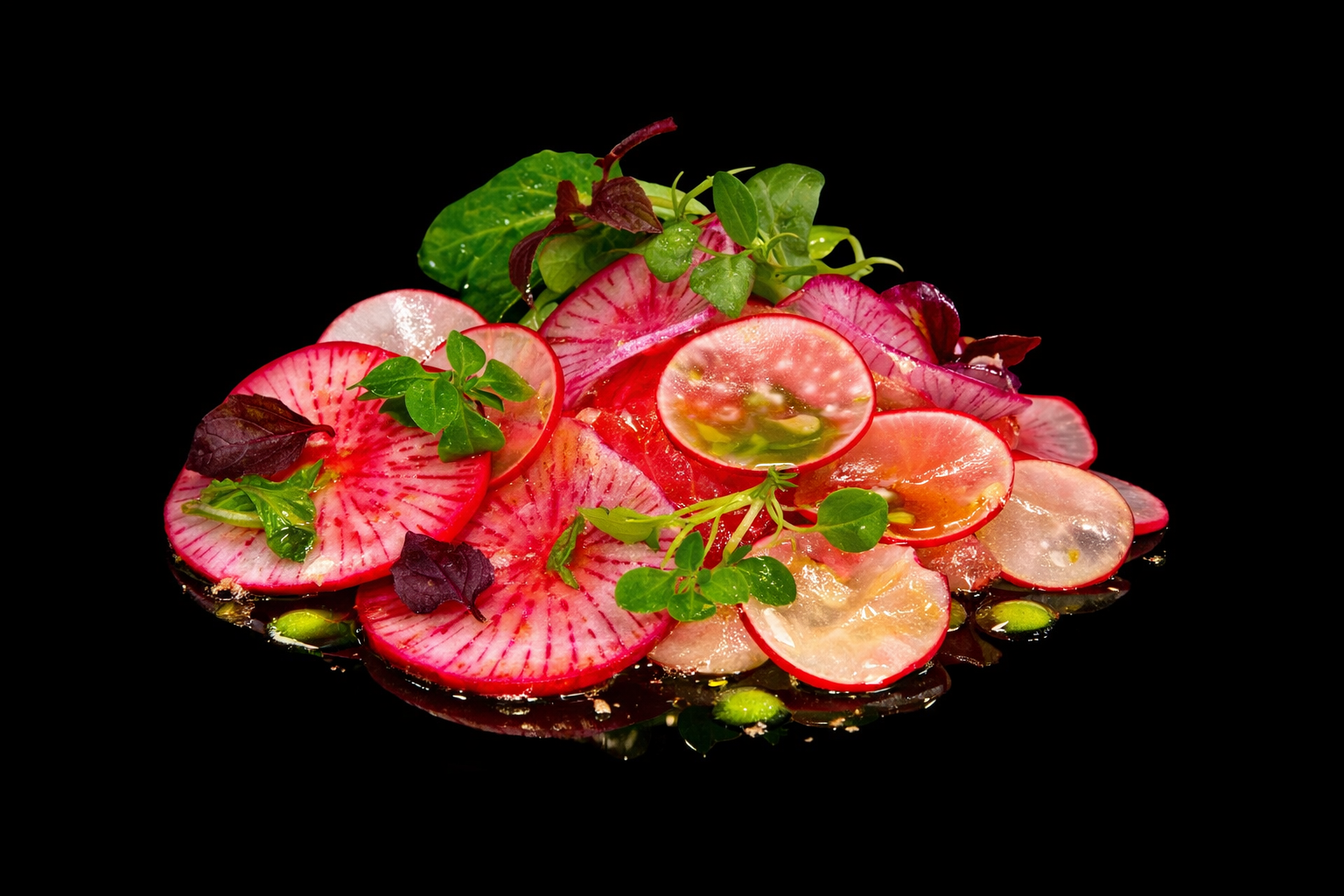 Assortiment de tranches de radis roses, avec différentes herbes vertes, présenté sur fond noir.