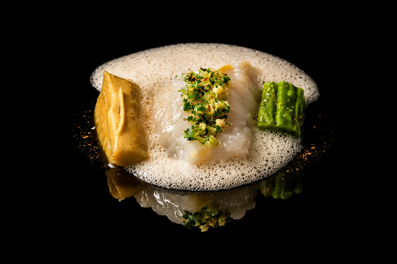 Assiette de poisson blanc avec des garnitures de légumes verts et une mousseline, sur fond noir.