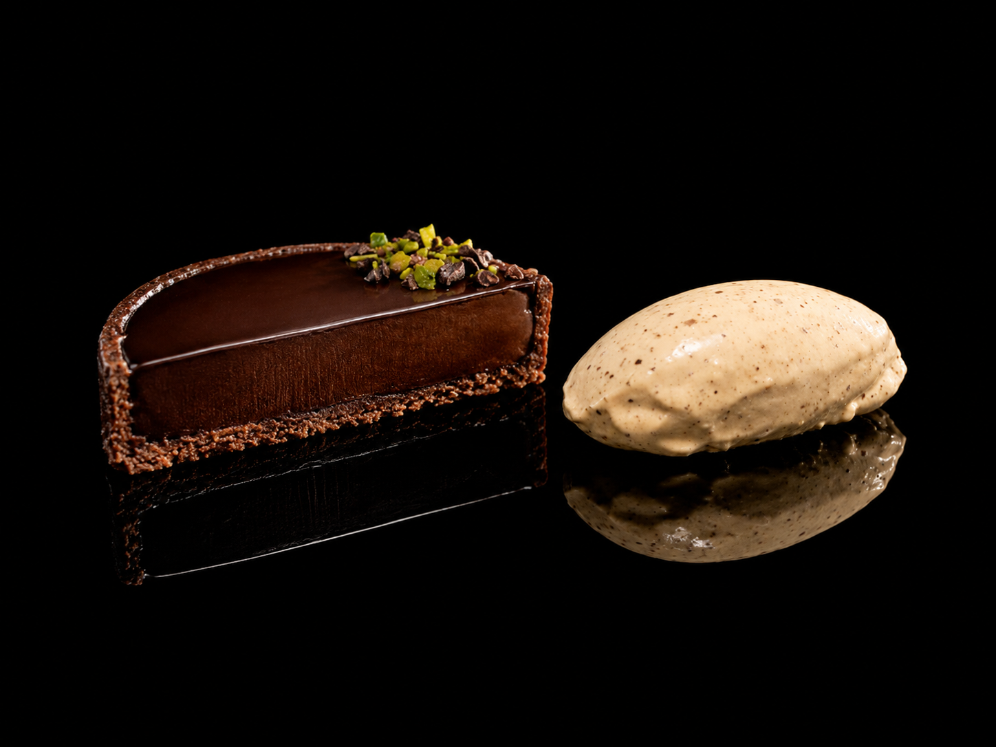 Gâteau au chocolat avec des pistaches et une boule de glace à la vanille sur un fond noir.