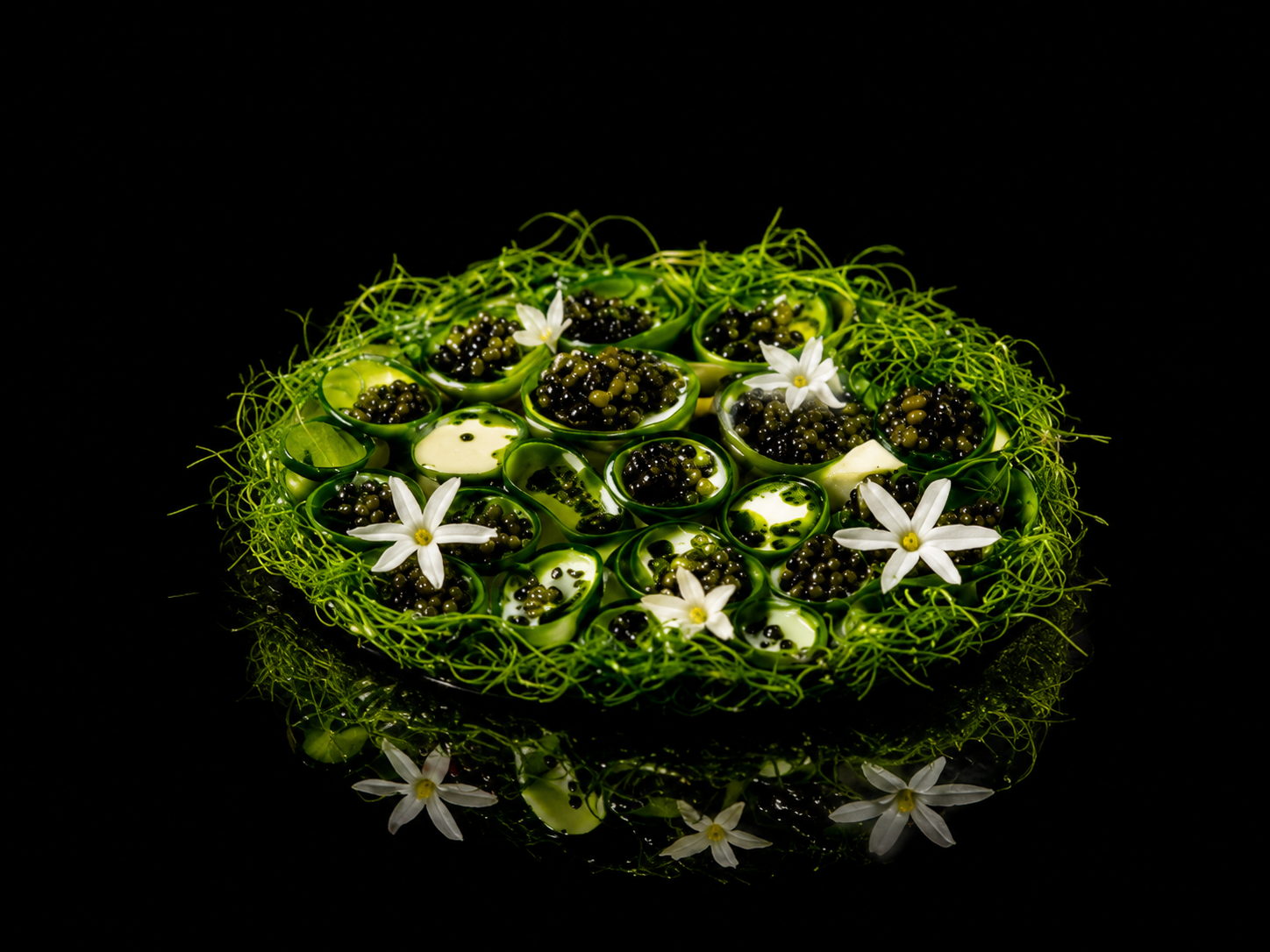 Arrangements de boules de gelatin vert avec des petites perles noires, décoré de fleurs blanches et de feuillage vert, sur un fond noir.