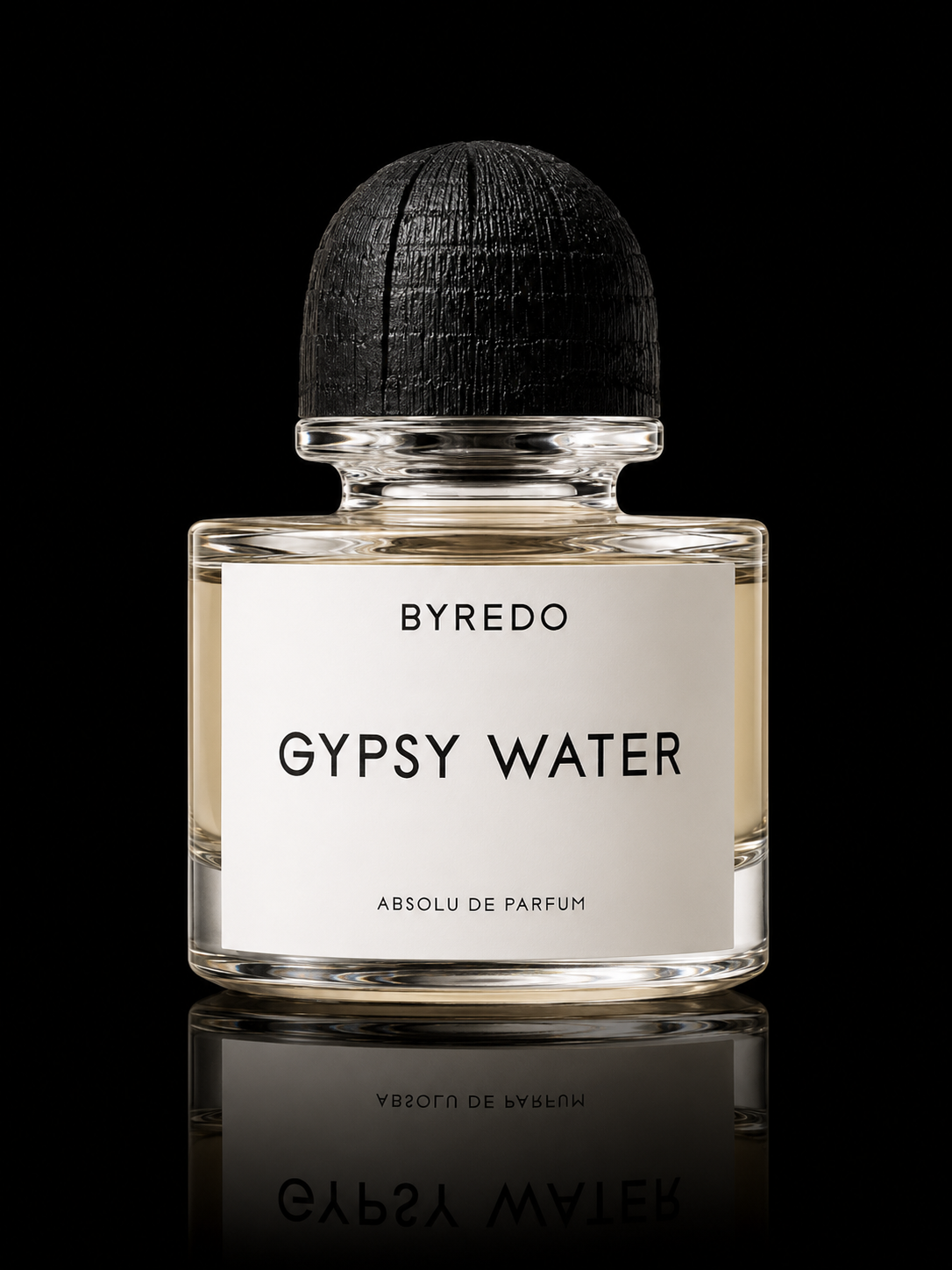 Flacon de parfum transparent avec bouchon en bois noir, étiquette blanche avec texte noir indiquant BYREDO GYPSY WATER ABSOLU DE PARFUM, posé sur une surface noire avec reflet.