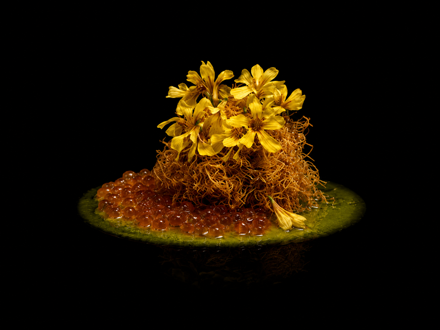 Présentation culinaire avec des fleurs jaunes, des œufs de poisson orange et une sauce verte sur fond noir.