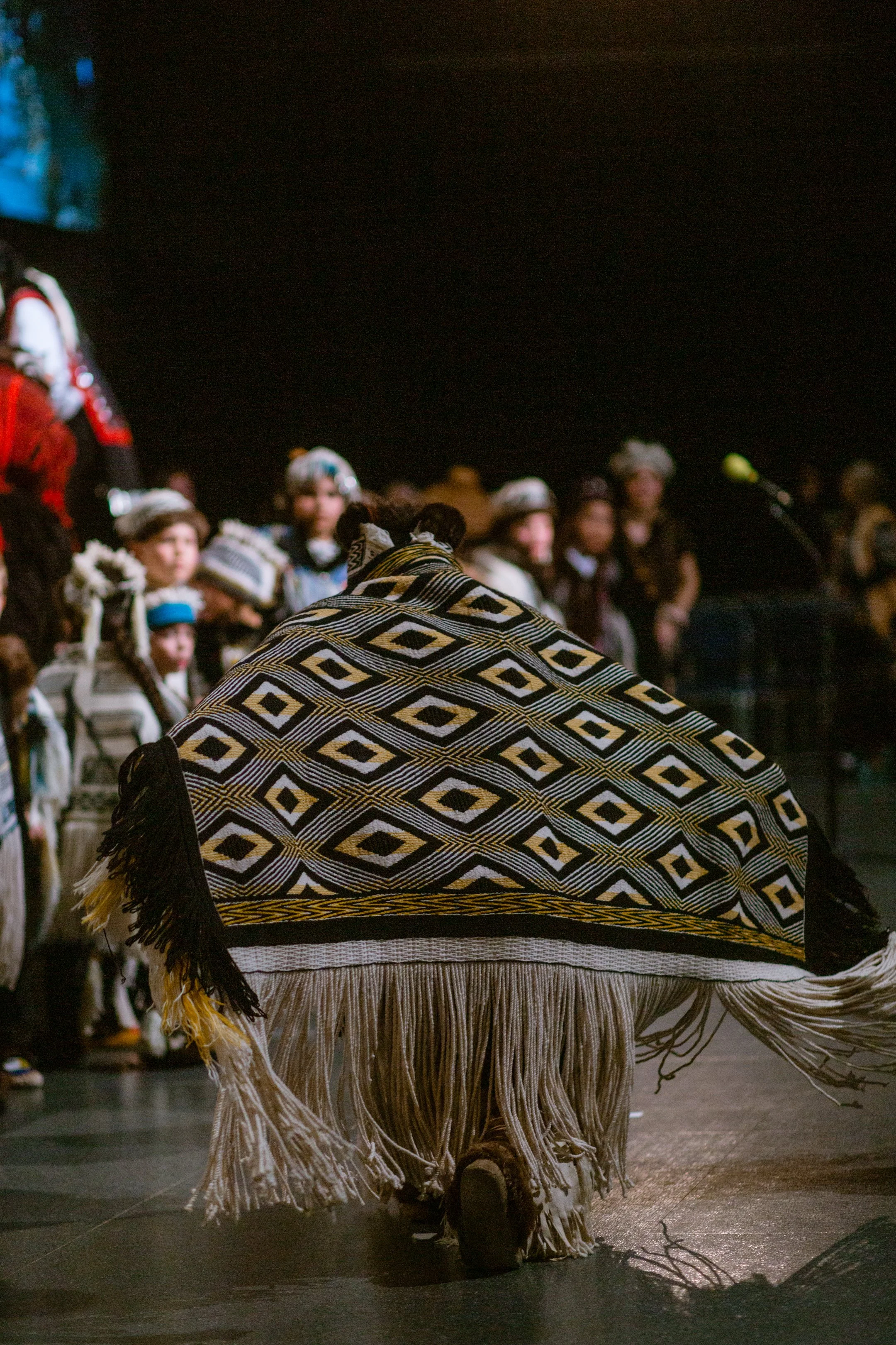 Person in traditional Tlingit Ravenstail robe performing a dance in front of an audience at a cultural event.