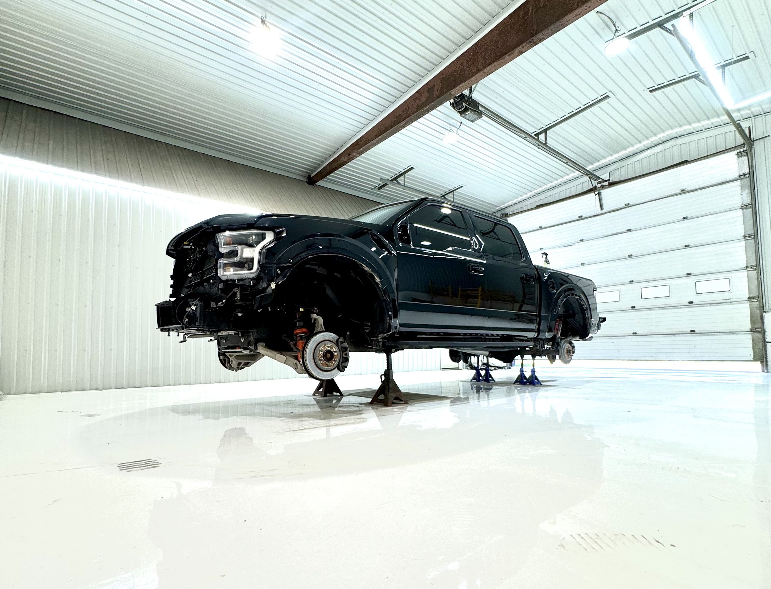 A black Ford Raptor pickup truck lifted on jack stands inside a spacious garage, with no wheels attached.