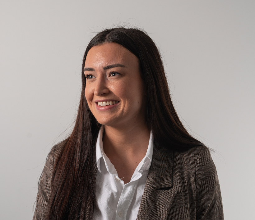 A smiling woman with long dark hair wearing a white shirt and a checkered blazer against a plain white background.