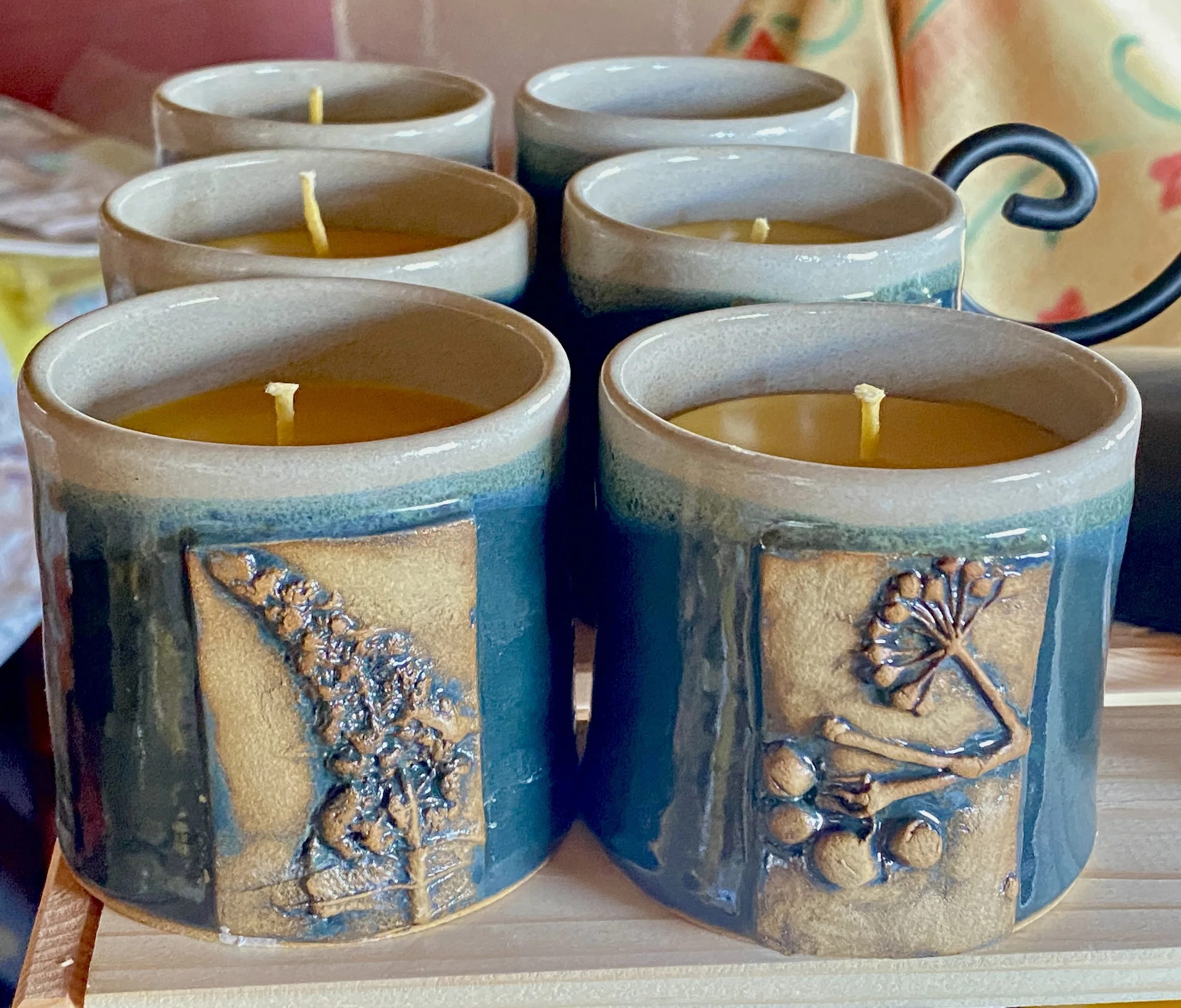 Six ceramic mugs filled with yellow candles on a wooden surface.