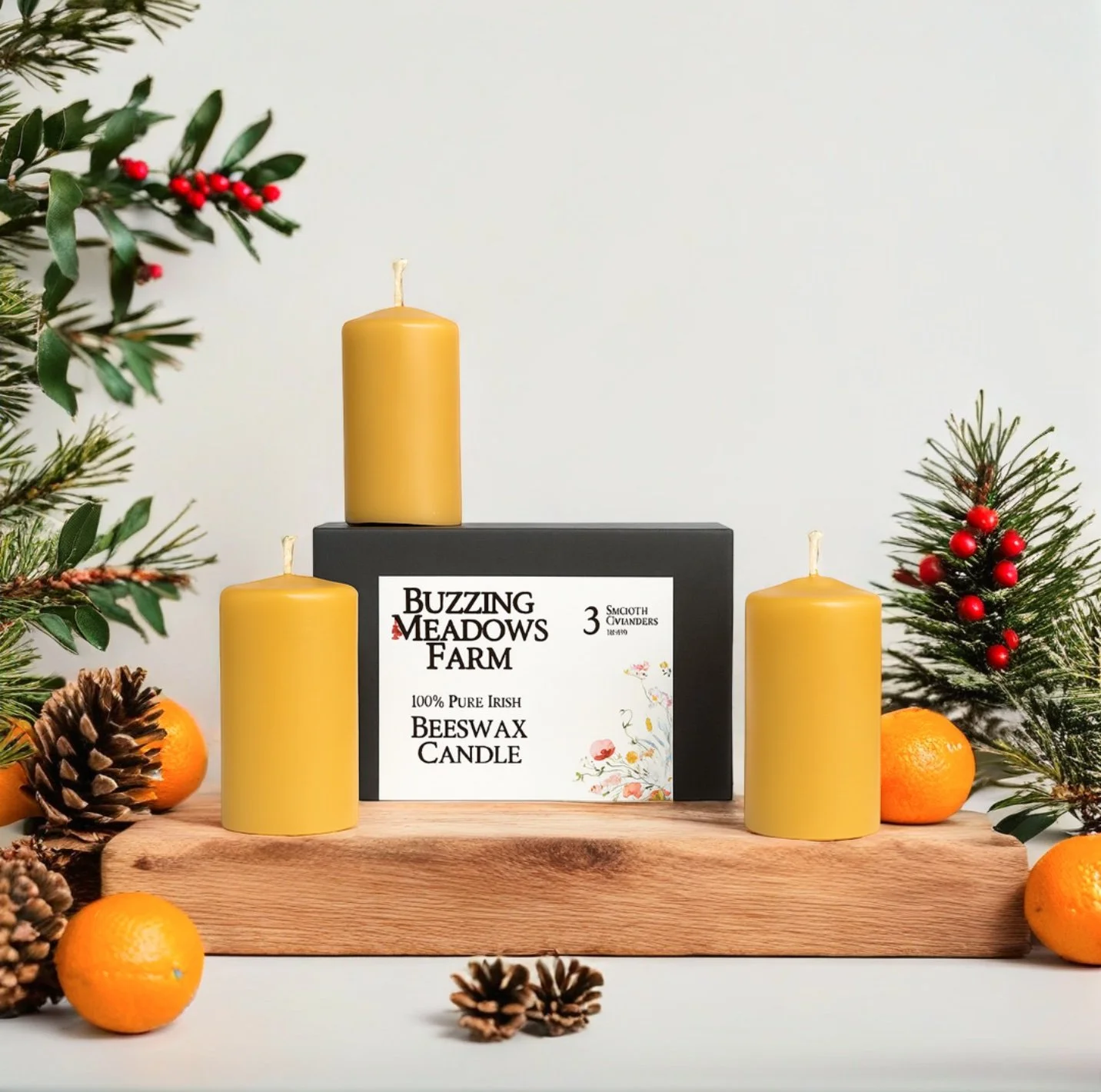 A display of three yellow beeswax candles on a wooden surface with pinecones, oranges, and Christmas greenery, with a box labeled 'Buzzing Meadows Farm 100% Pure Irish Beeswax Candle' in the background.