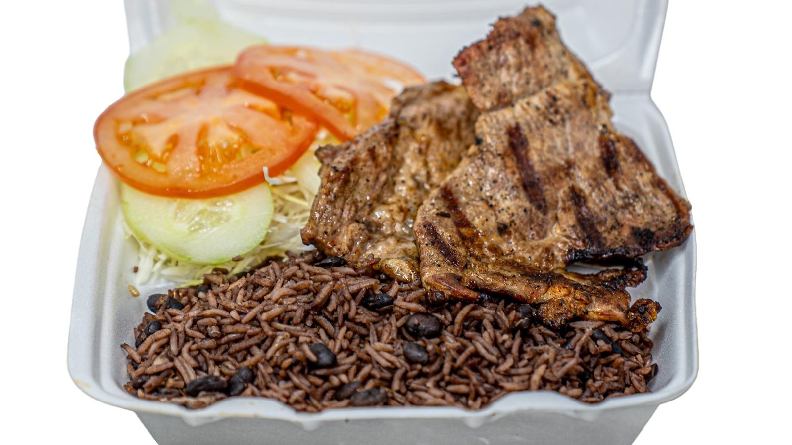 A styrofoam takeout container with grilled pork ribs, seasoned rice, sliced tomatoes, and cucumber slices.