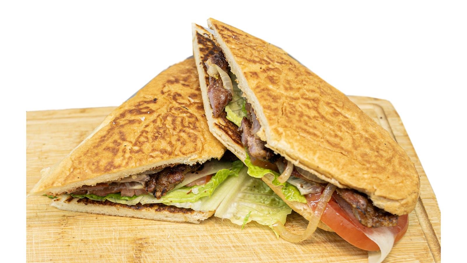 Two sliced toasted sandwiches with lettuce, tomato, onions, cheese, and cooked meat, served on a wooden cutting board.