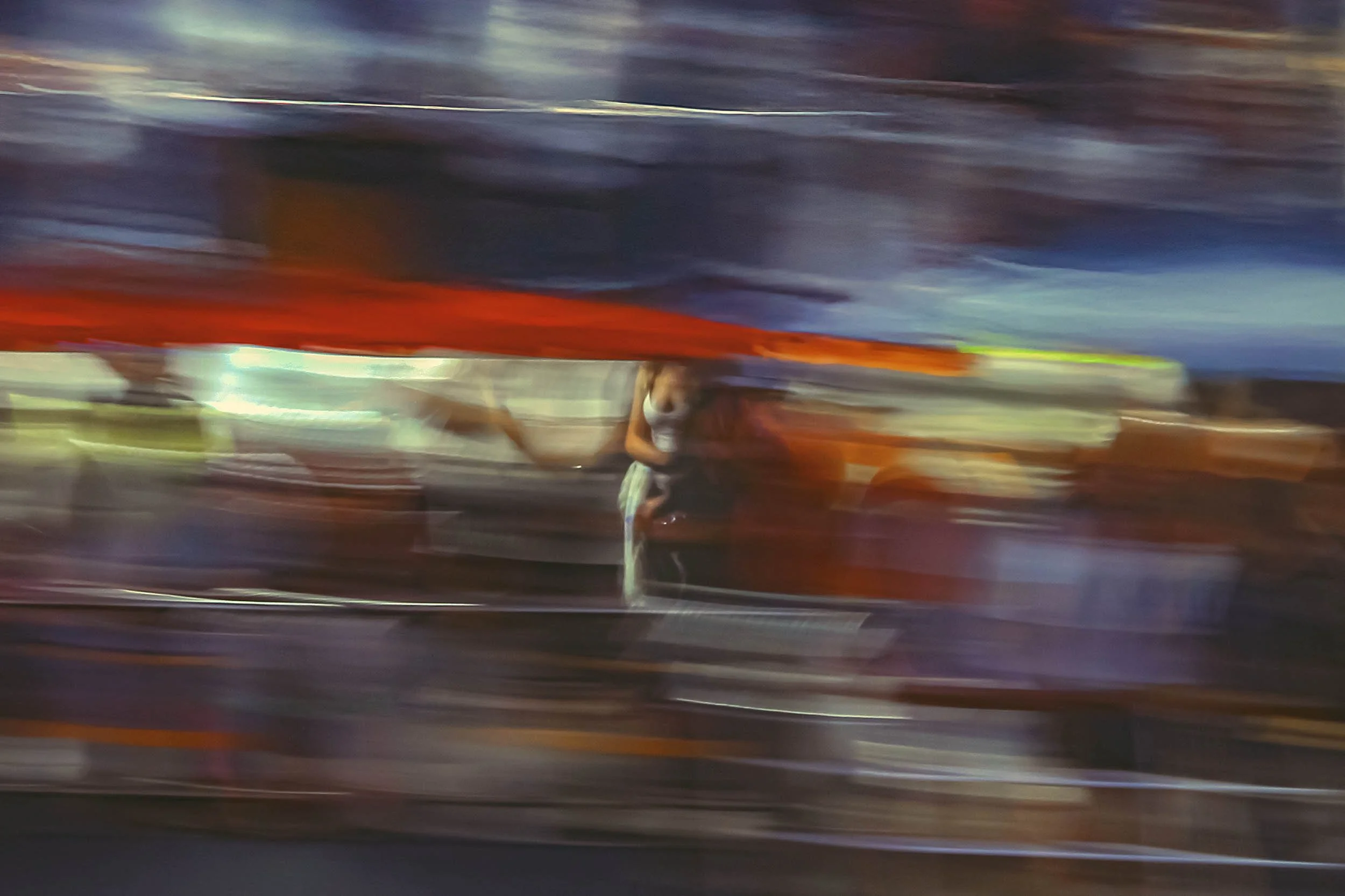 Blurred motion image of a person riding a horse at sunset or sunrise, with a dramatic sky and horizon in the background.