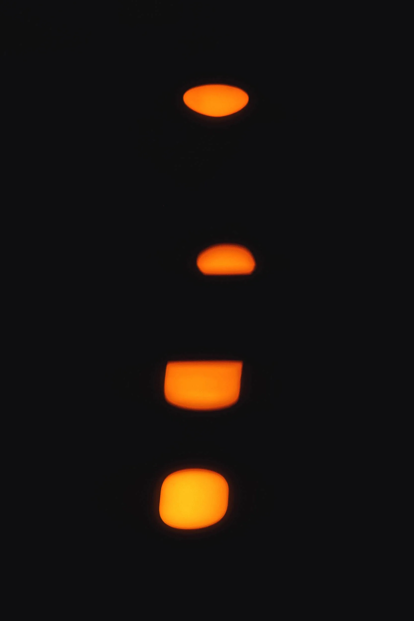 The image shows a vertical sequence of four orange, semi-oval lights against a black background, possibly reflecting on a surface.