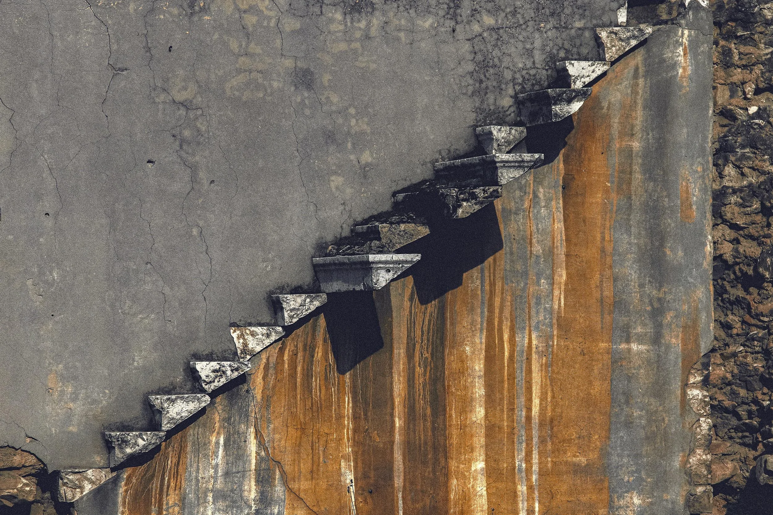Close-up of metal stairs embedded in a cracked concrete surface with rusted steel and gravel around.