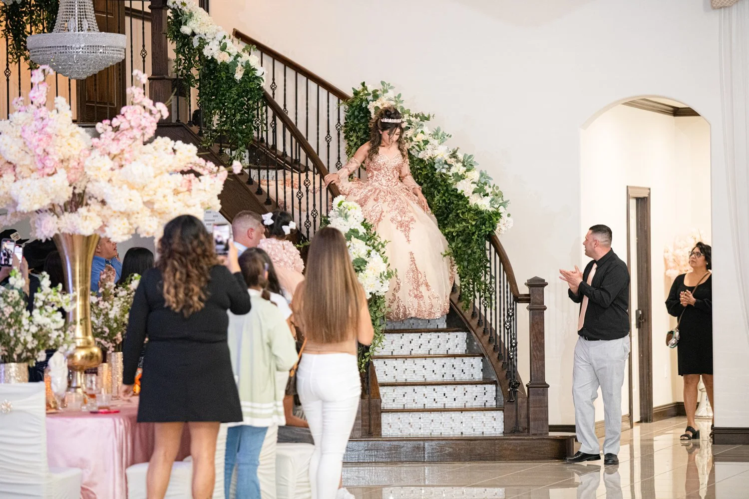 Quinceañera making her grand staircase entrance in an elegant ballroom as family and guests watch and celebrate her special moment