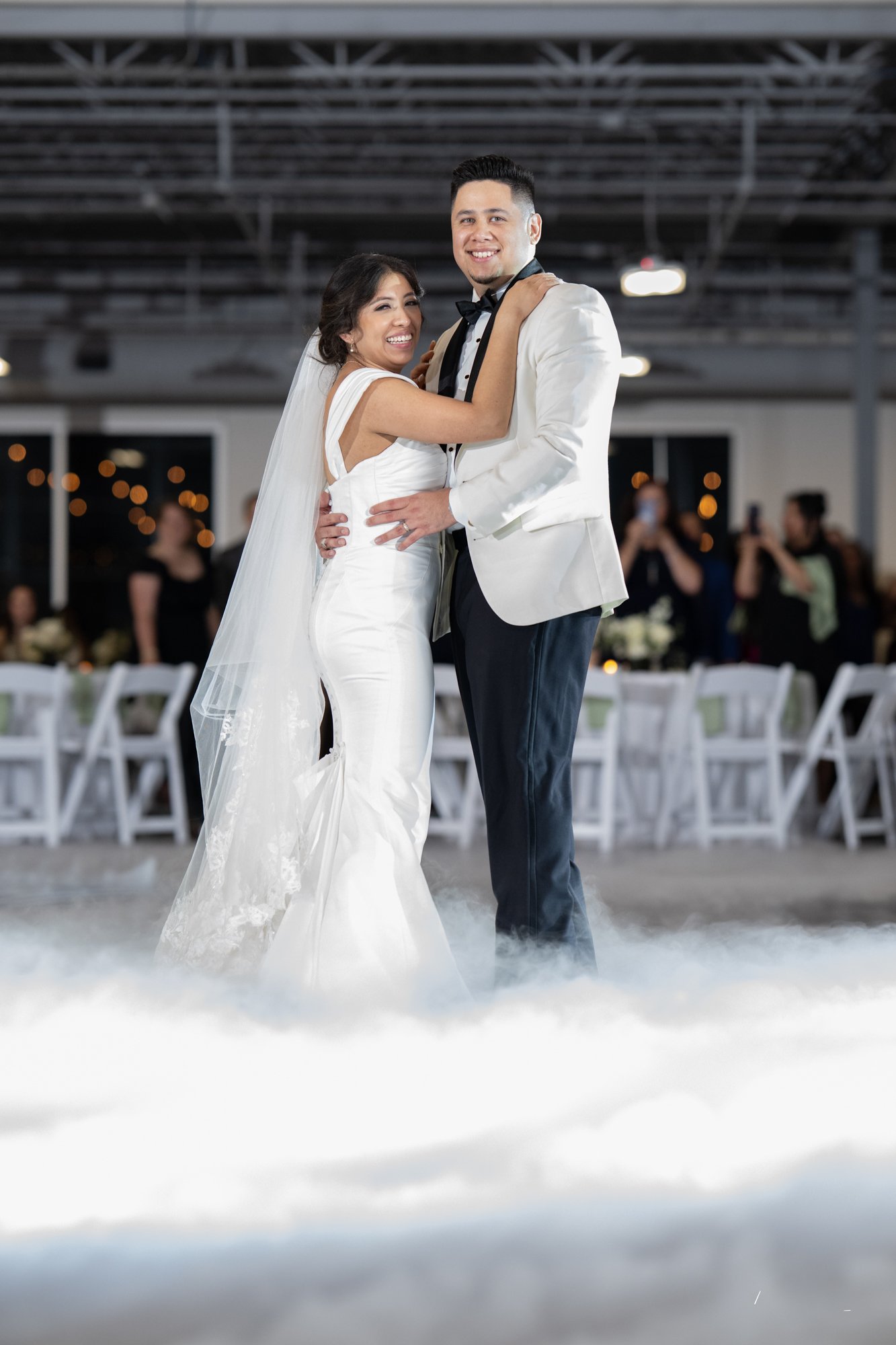 Briseida and Sergio share their first dance as husband and wife during their Dallas, Texas wedding reception, surrounded by dancing on a cloud effects and family celebrating their special day.