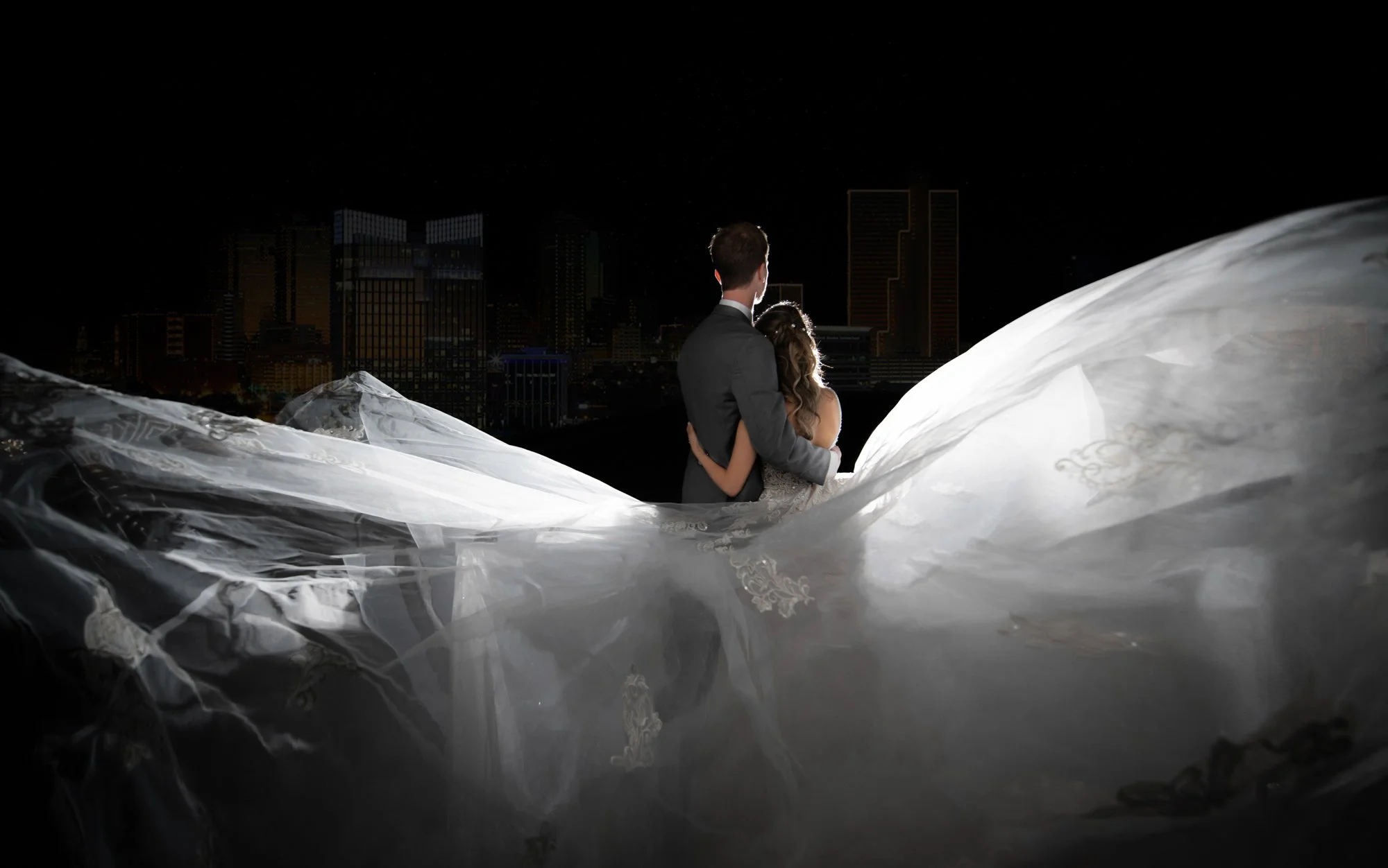 Luxury wedding couple portrait at night with flowing veil and city skyline background