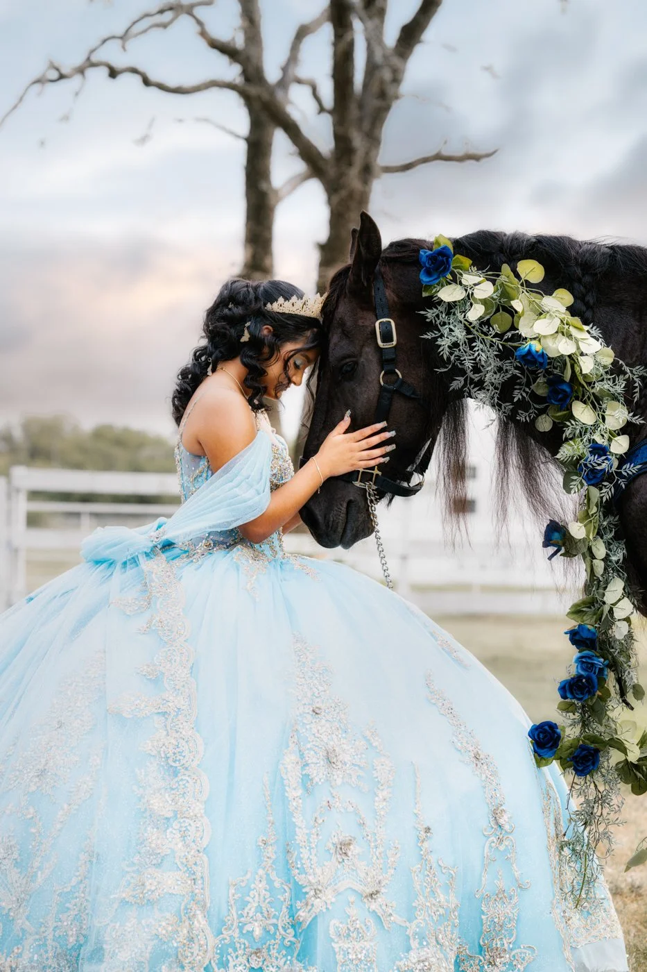 Quinceañera portrait of a young woman in a blue gown gently posing with a horse.