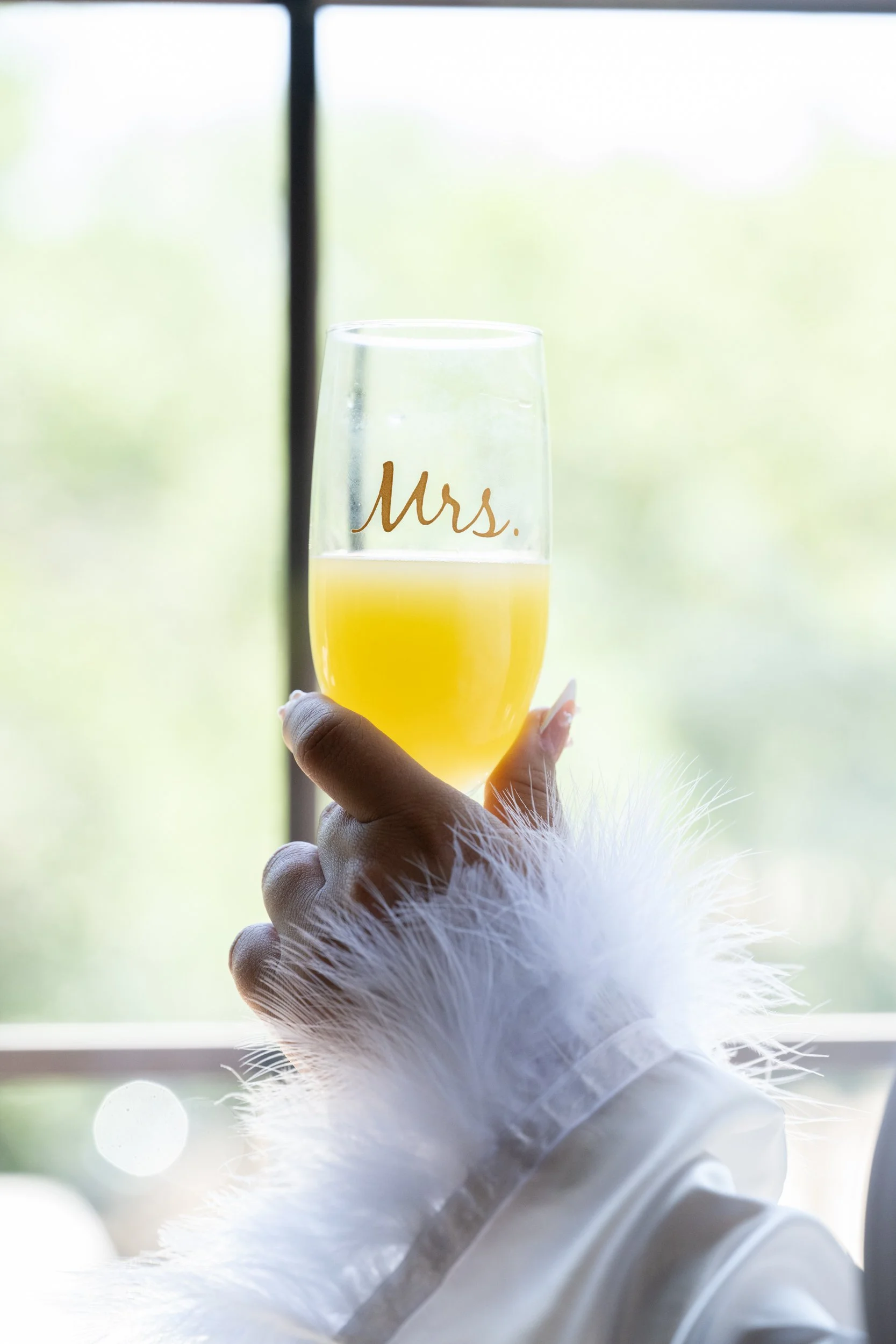 A refined bridal getting-ready moment as the bride raises a personalized “Mrs.” glass, capturing anticipation, joy, and elegance before the ceremony begins.
