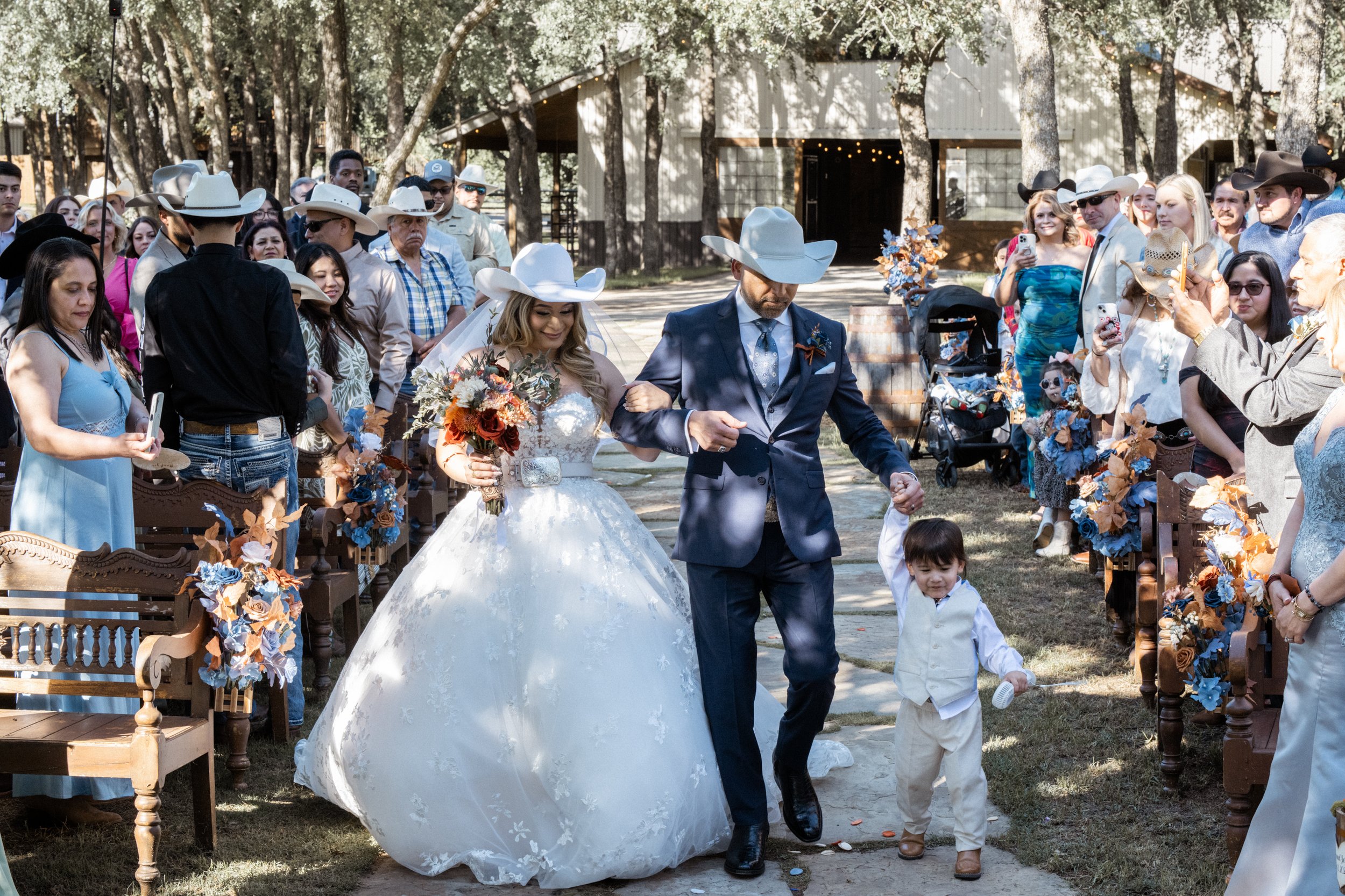 “The bride is escorted down the aisle by her father, surrounded by family and loved ones, capturing a deeply emotional moment that honors tradition, love, and the powerful bond between parent and child.”