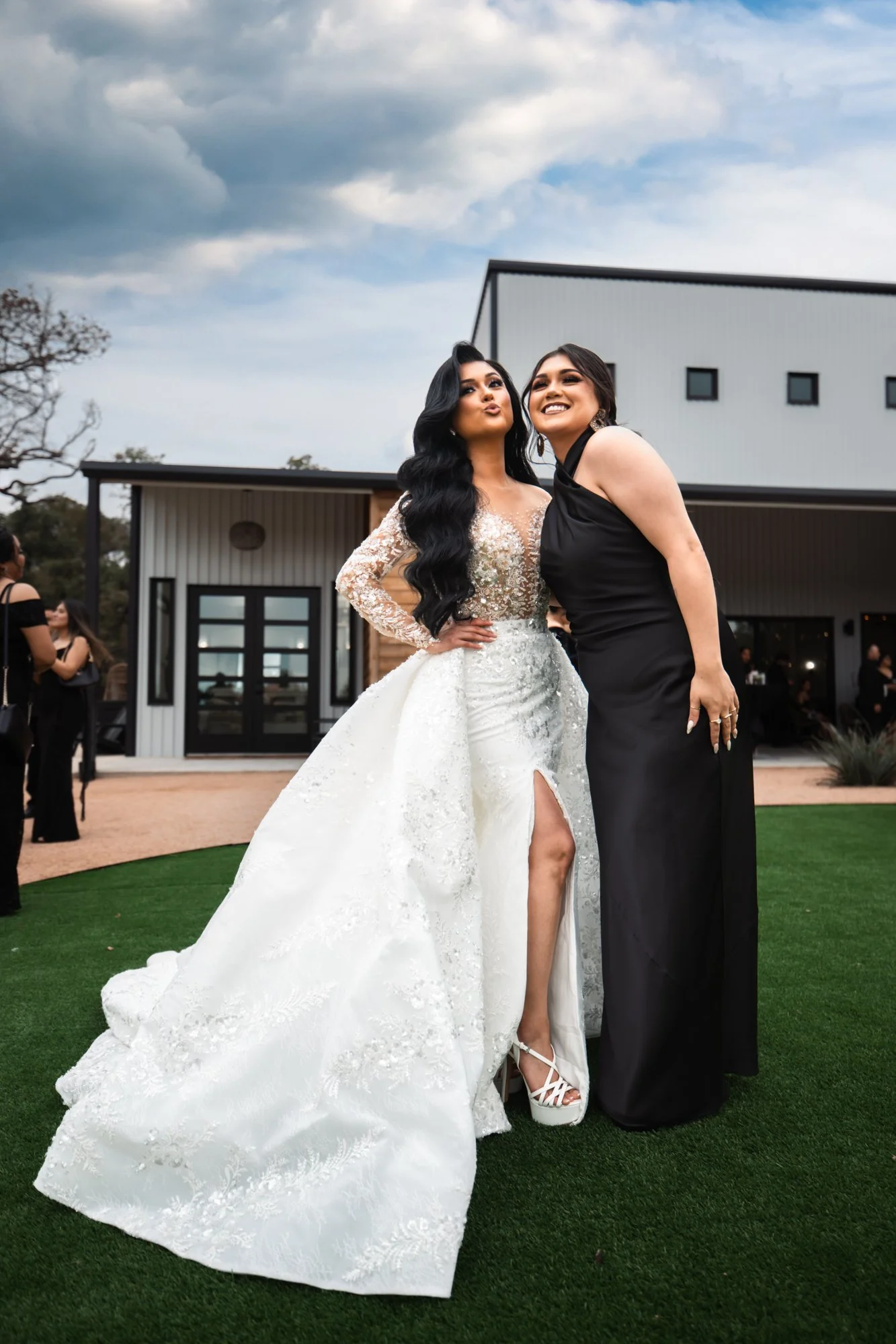 The bride poses joyfully with her sister, showcasing her elegant lace wedding gown and confident personality as they share a lighthearted moment during the celebration.