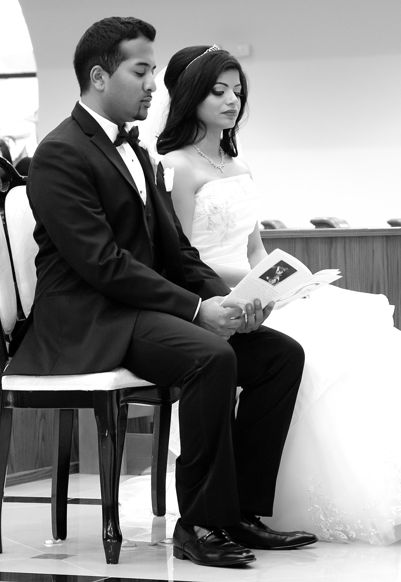 A tender ceremony moment shows the bride and groom seated together, reading during the service. Their calm expressions reflect reflection, commitment, and the emotional weight of the vows being exchanged.